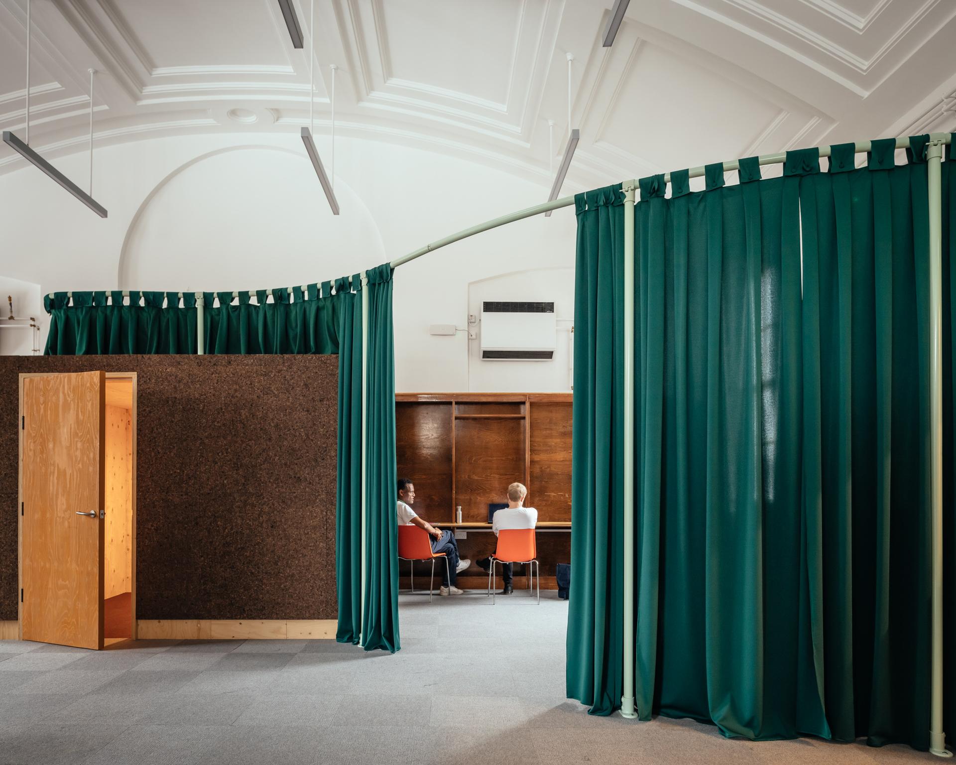 A sustainable room with green curtains and a couple of people sitting at a table, designed with modular timber construction elements.