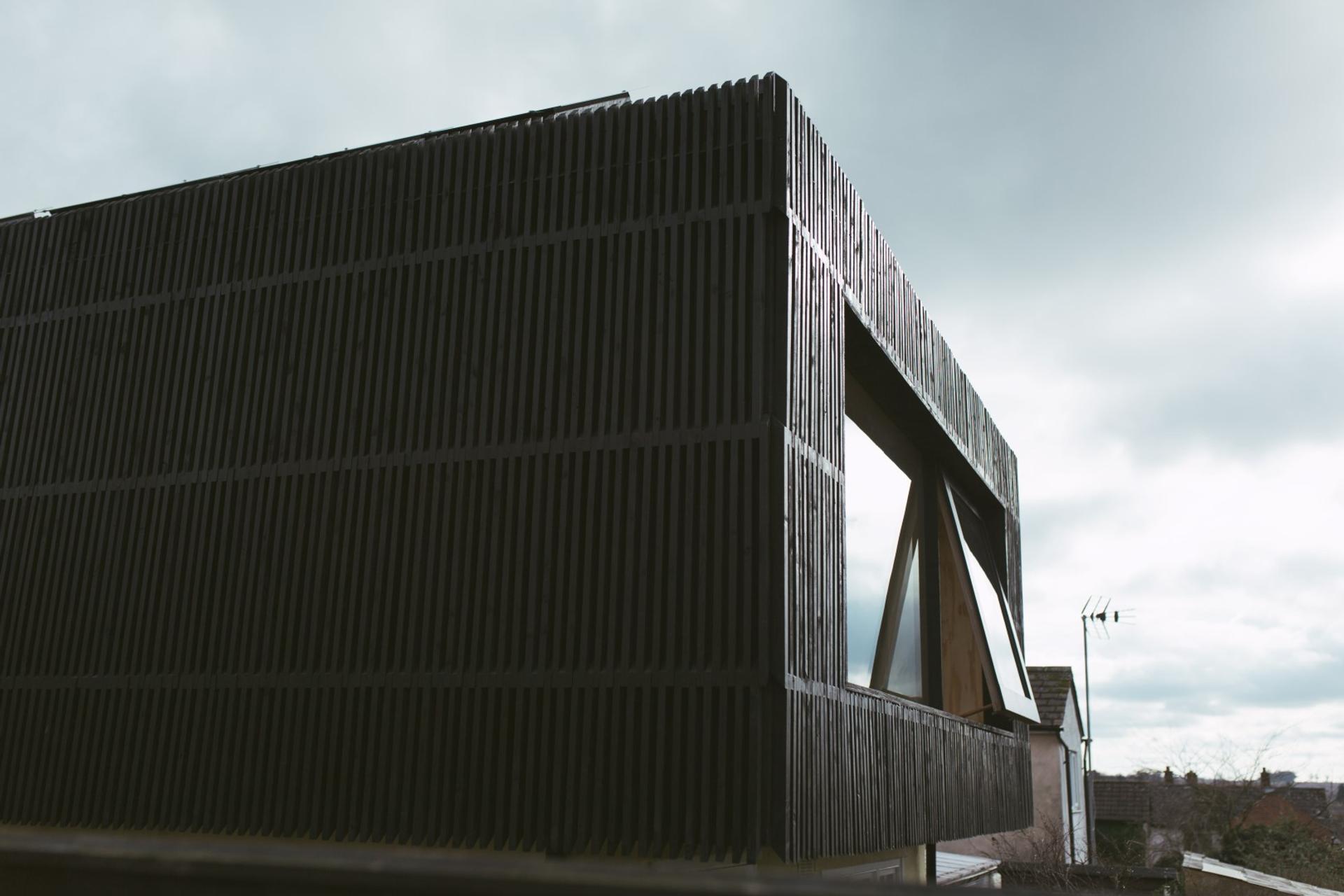 A U-Build black timber clad extension to the rear of the cottage house with an open window