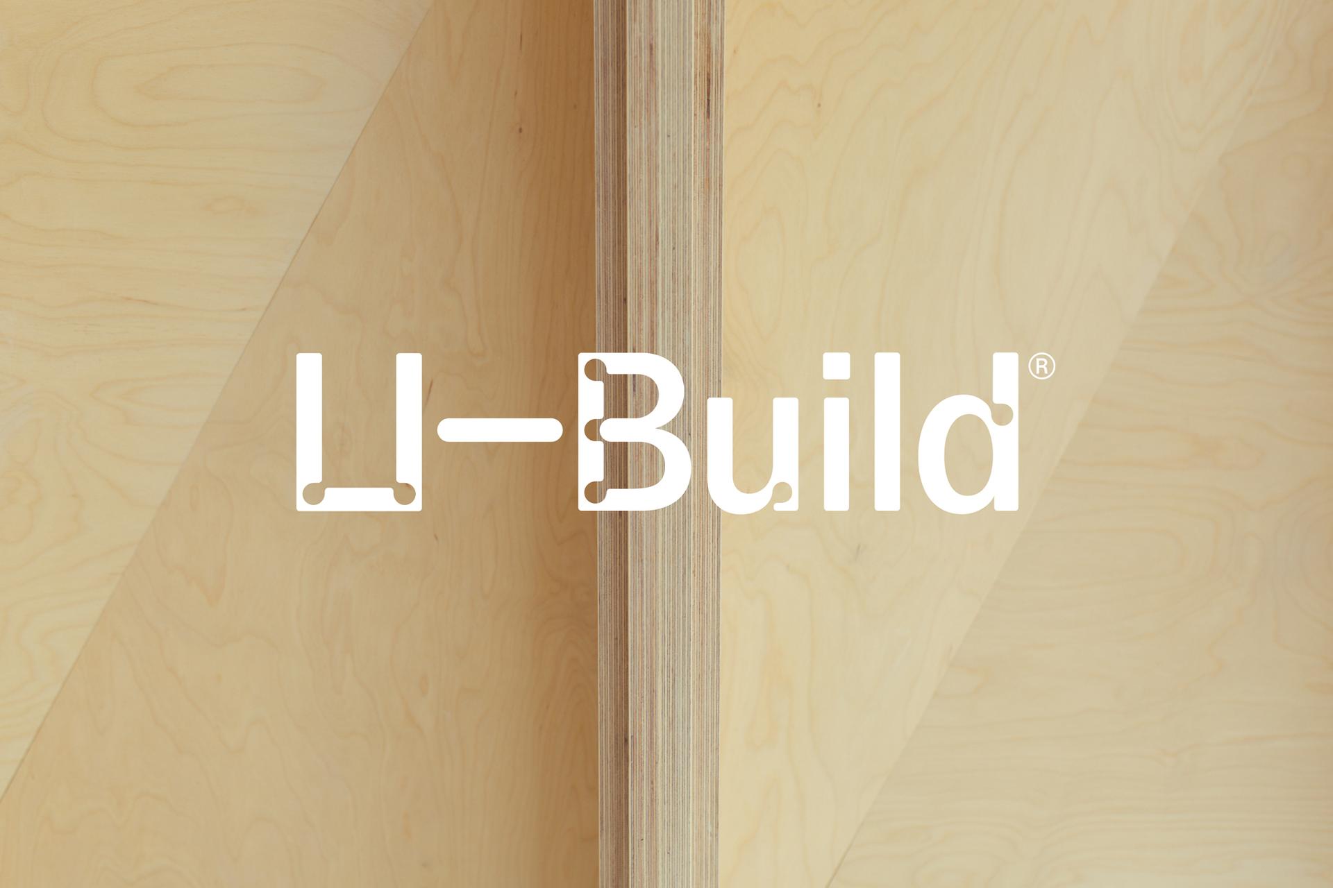 The image shows a light birch wood background with the white U-Build® logo in the centre, featuring a stylised U and bold lettering, reflecting the brand’s modular and sustainable approach.