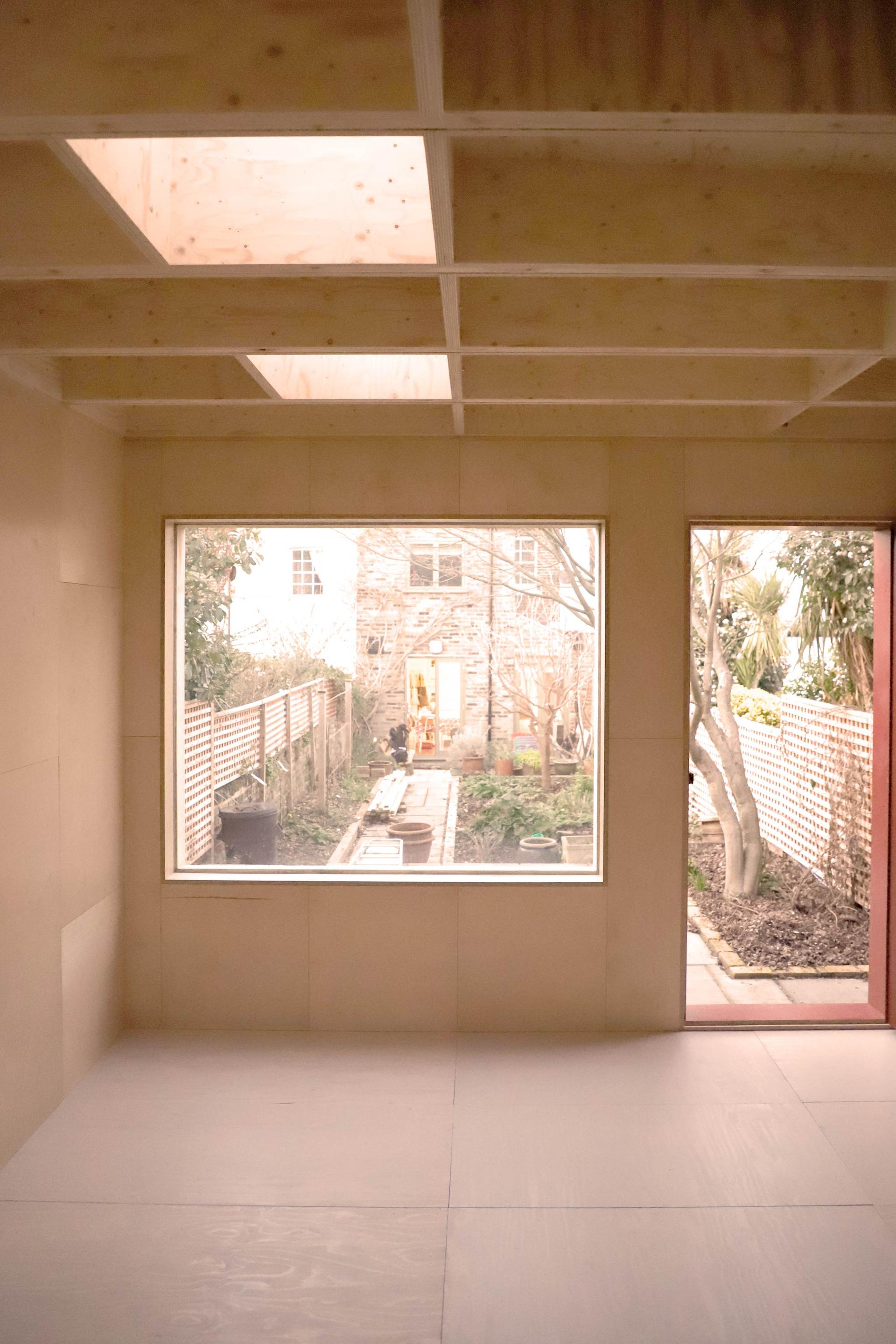 Inside a U-Build garden studio in East London with wooden walls featuring the front window and the door.