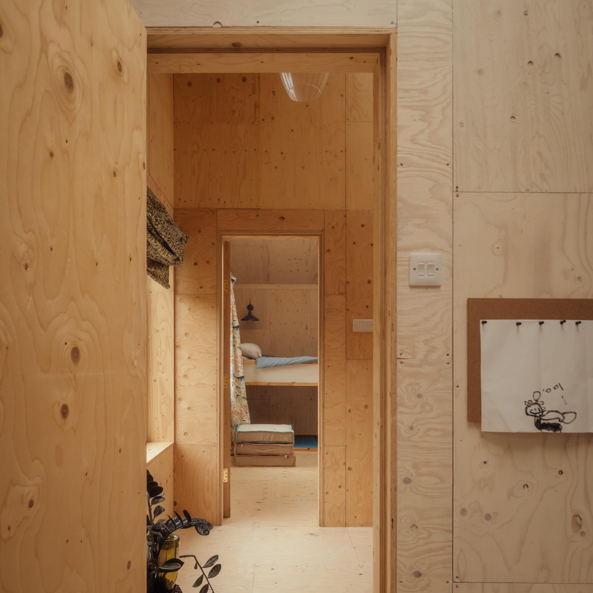 A view through two doorways in a room with light timber cladding, showing a bedroom with a bunk bed in the background.
