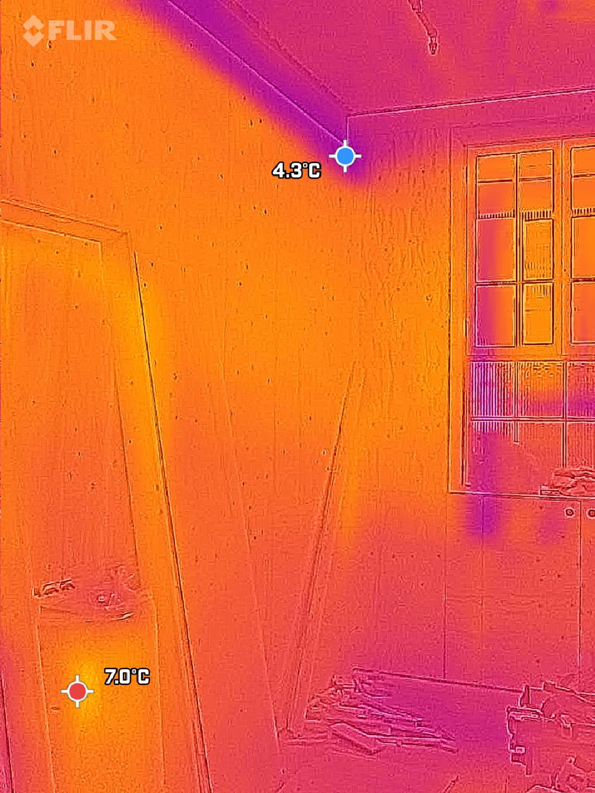Thermal image of a room with a window and spruce boards leaning against the wall; colder area near the ceiling (4.3°C) and warmer spot at the bottom left (7.0°C).