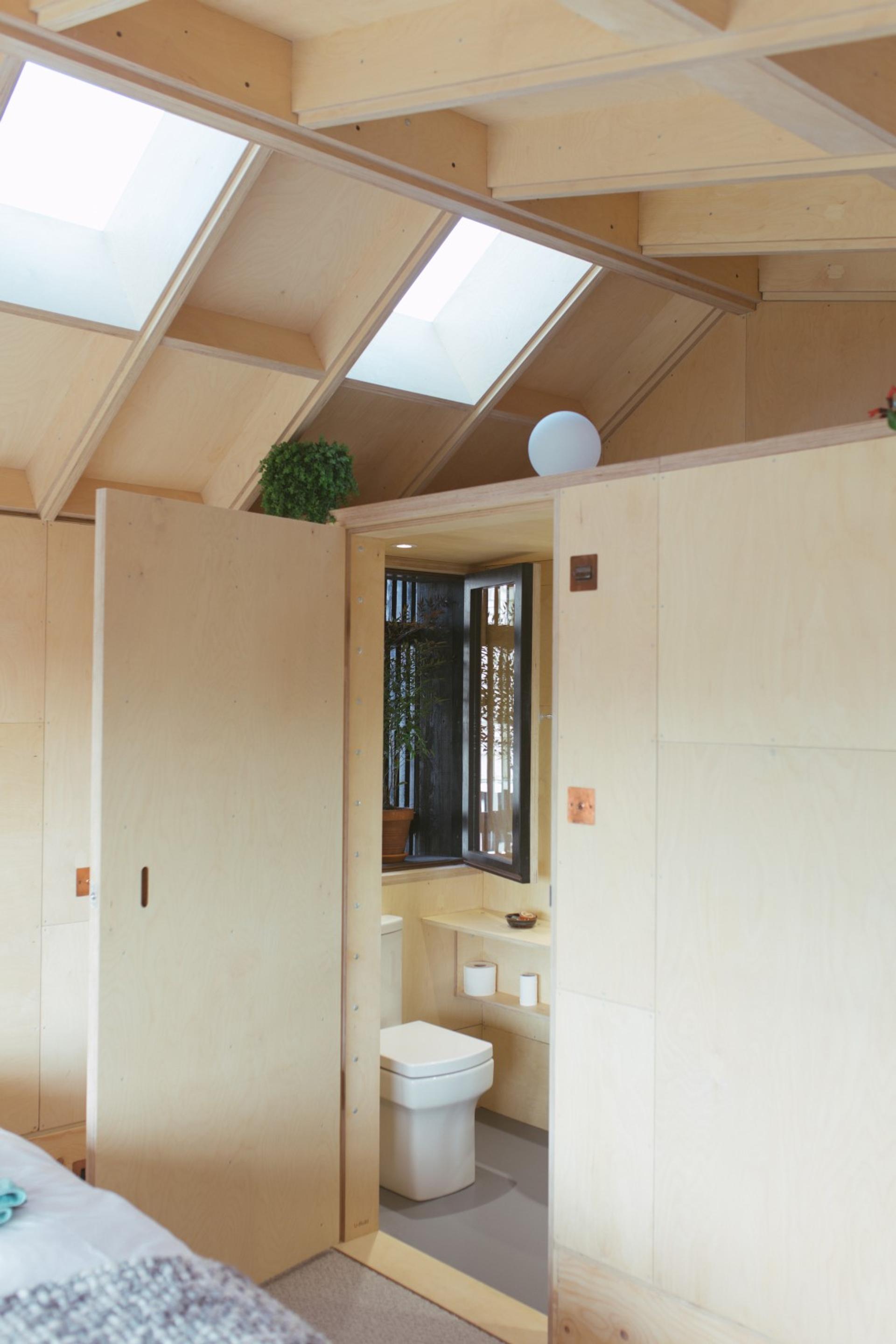 A wooden bathroom pod inside the bedroom with a skylight
