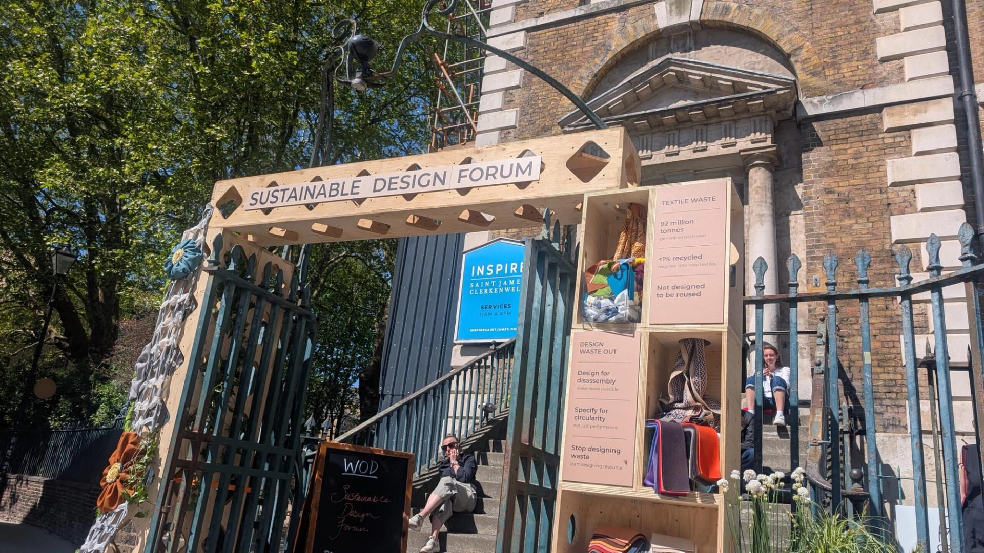 Wooden archway labelled Sustainable Design Forum marks the Threshold of Change at a brick building entrance, featuring posters on textile waste and sustainability, with colourful fabric samples in this art installation.