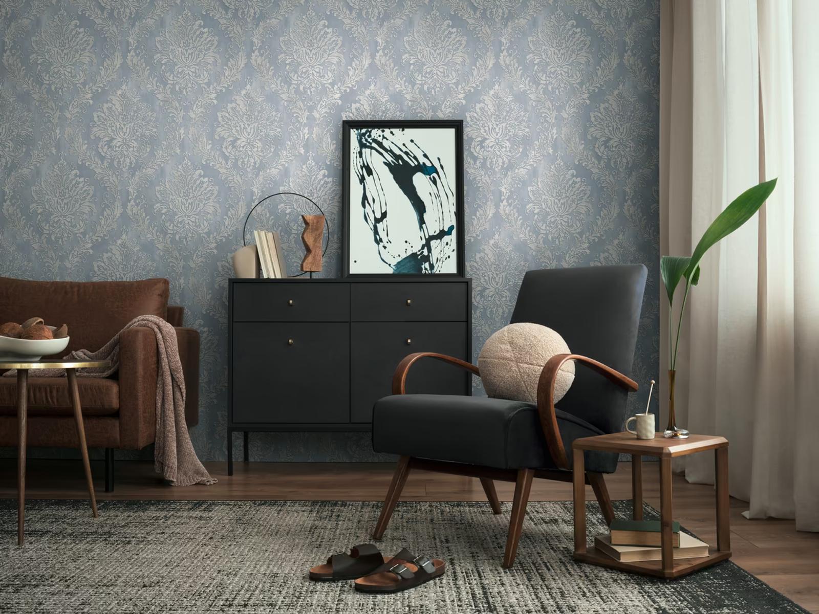 Blue Damask wallpaper behind a black sideboard and leather armchair