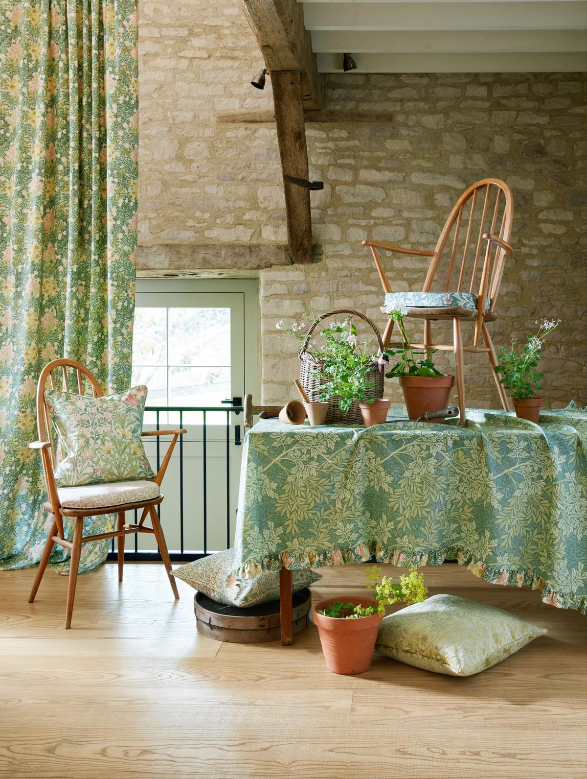 Morris floral curtains, a patterned tablecloth and cushions in a stone-walled room with wooden chairs