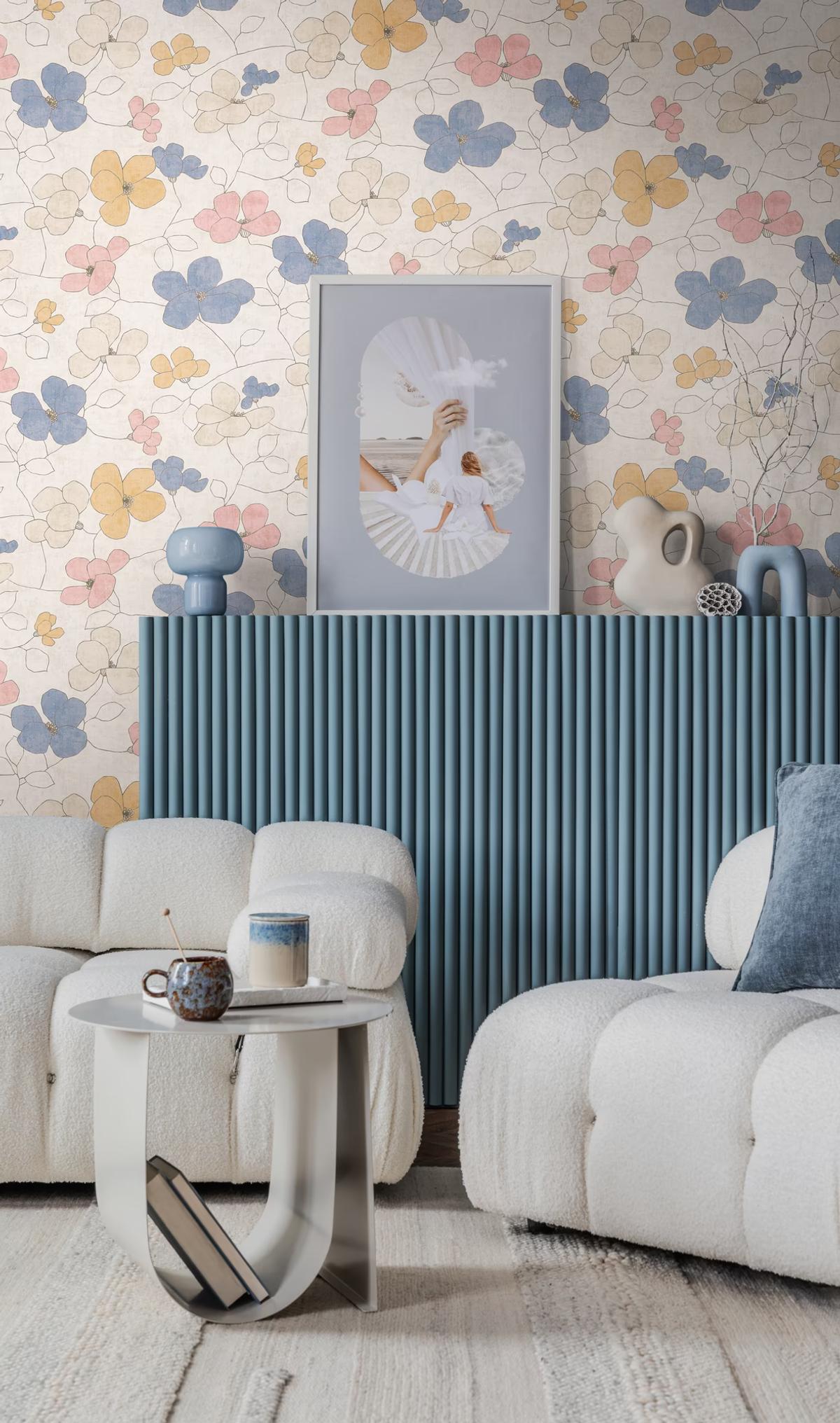 Wallpaper with outlined blossoms in blue, pink and ochre above a blue fluted sideboard and bouclé sofas
