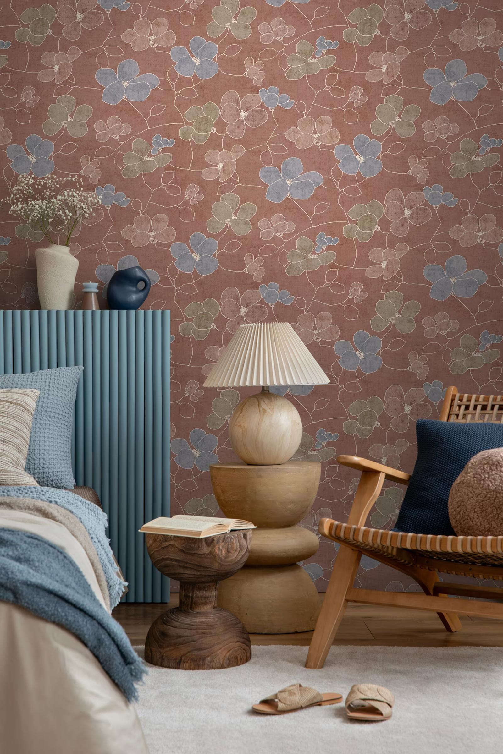 Rust Blossom wallpaper in a bedroom with a rattan chair and fluted blue headboard