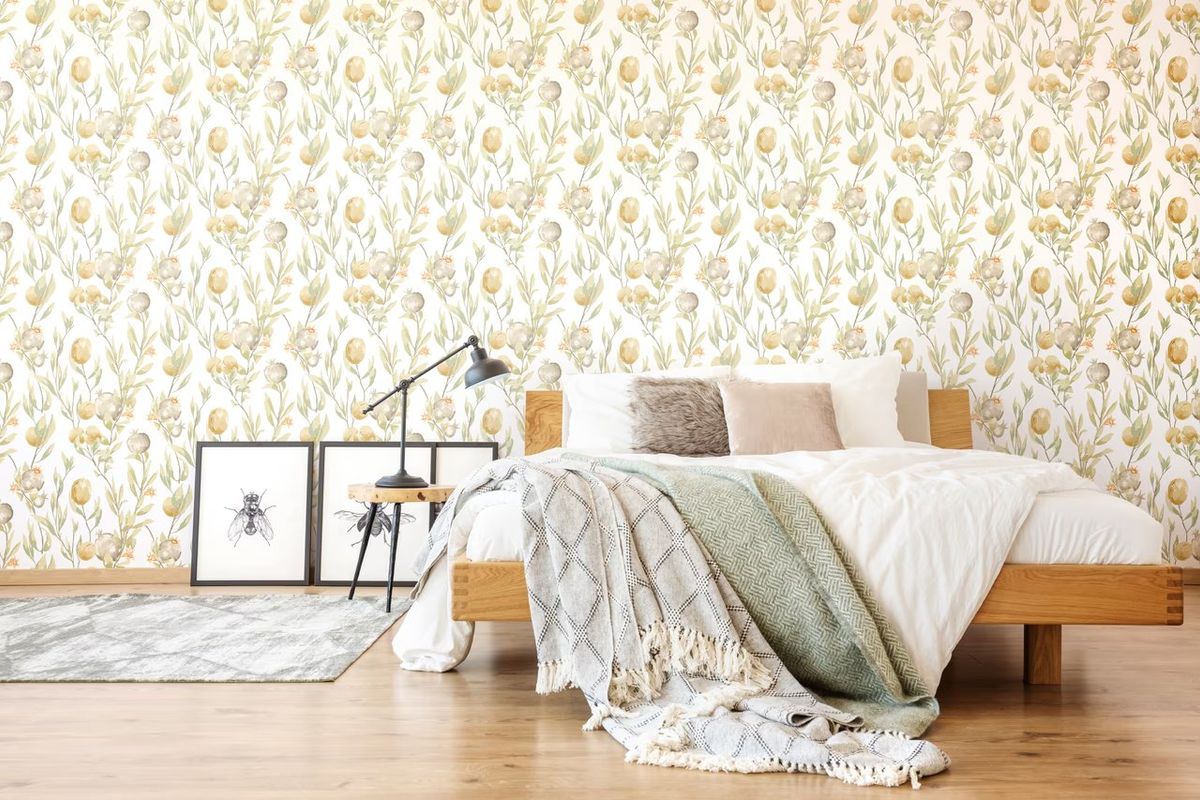 Pale ochre botanical wallpaper on a cream ground behind a wooden bed with a green throw