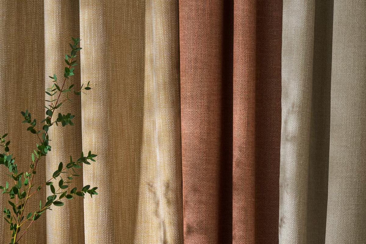 Folds of curtain fabric in gold, cream, terracotta and stone, with a eucalyptus sprig in front