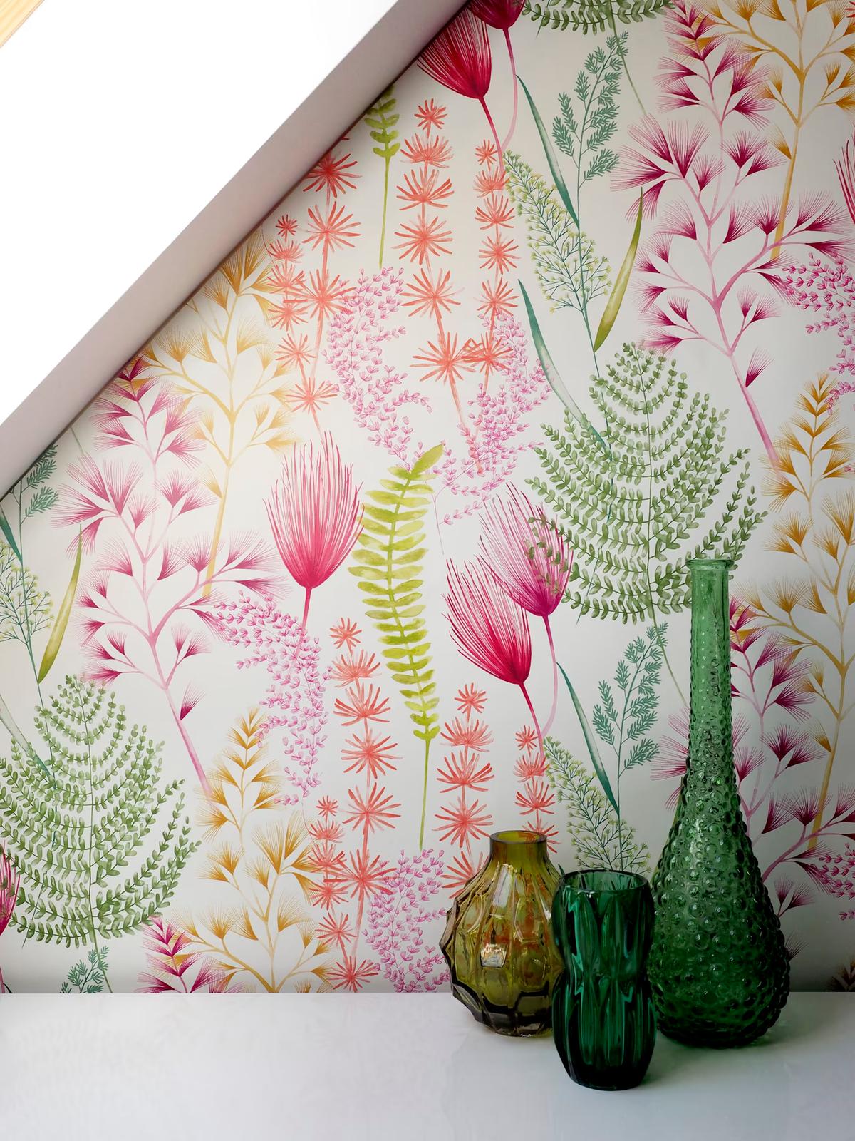 Watercolour fern and blossom wallpaper in coral pink and green under a sloping ceiling, with green glass vases