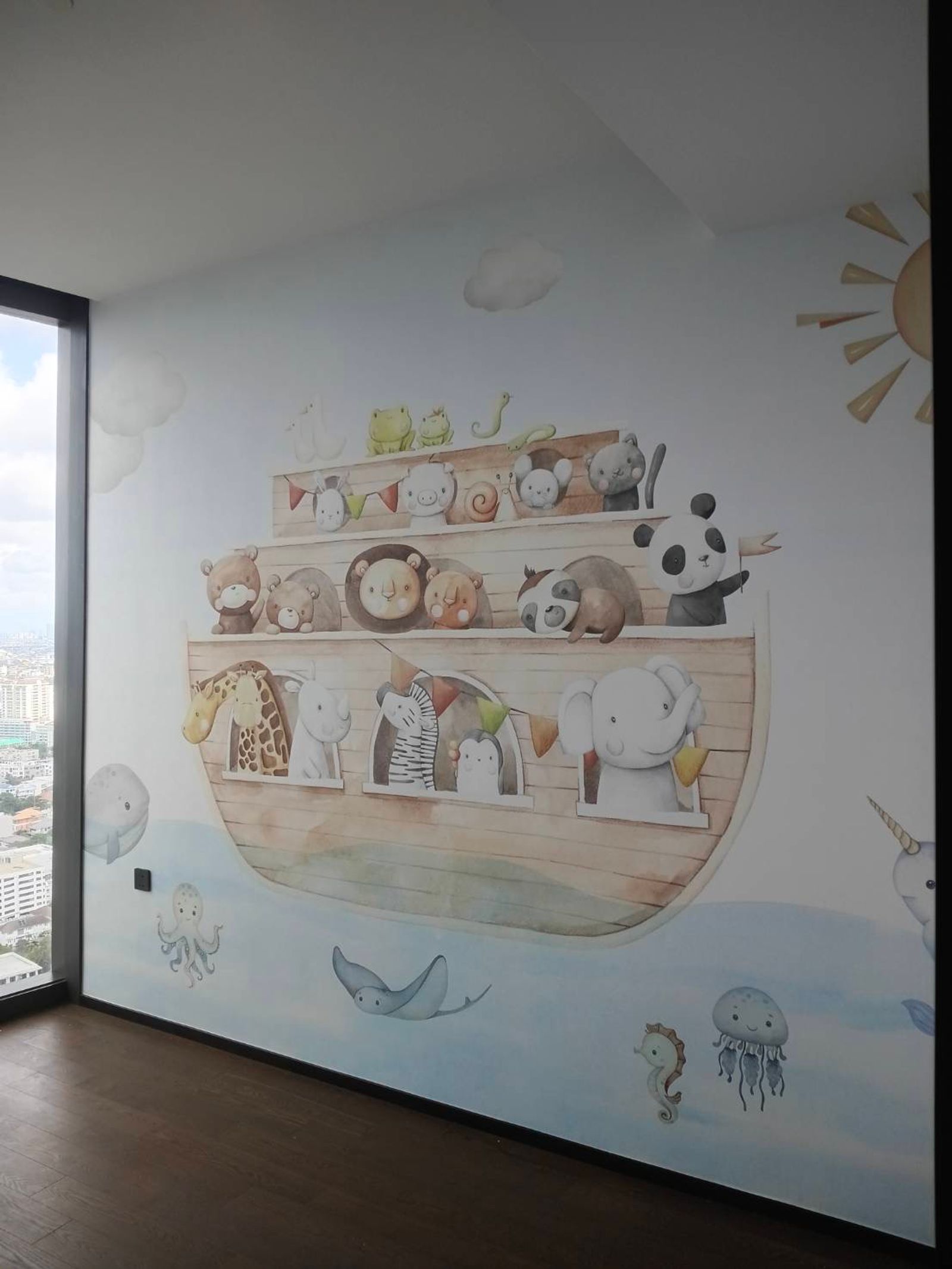The same mural wall seen from the window side, the city beyond the glass, with the sun and a narwhal at the far edge of the print