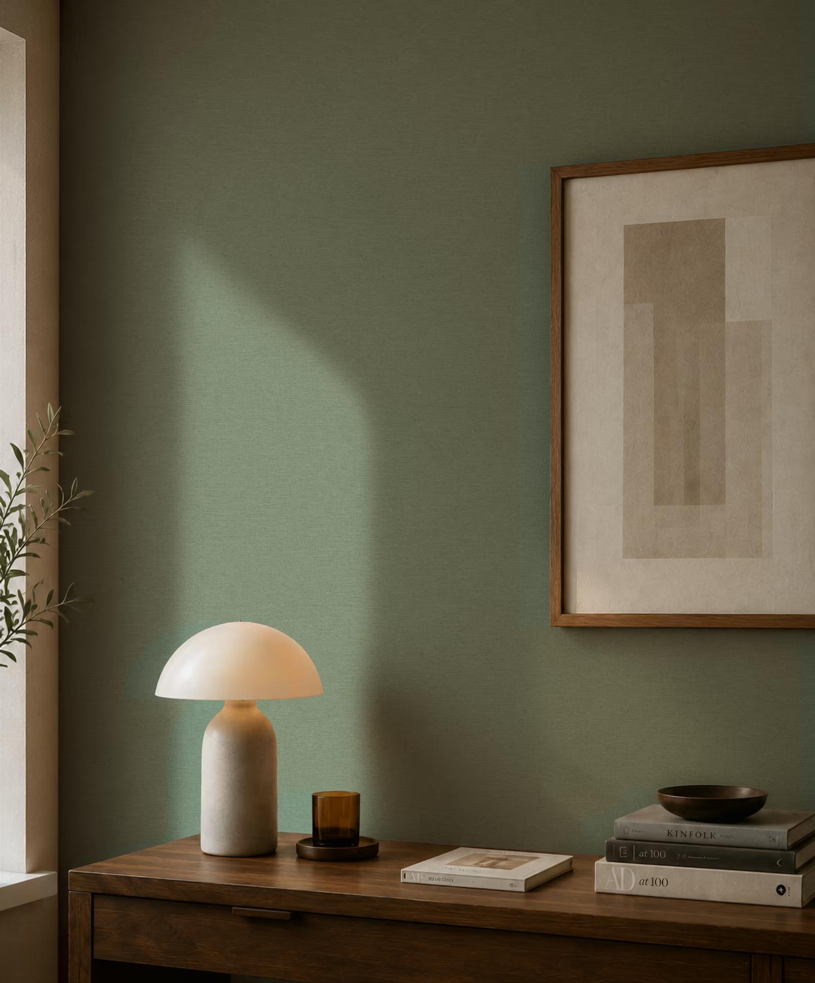 Sage-green linen-weave wallpaper catching daylight above a walnut sideboard with a stone lamp and framed print