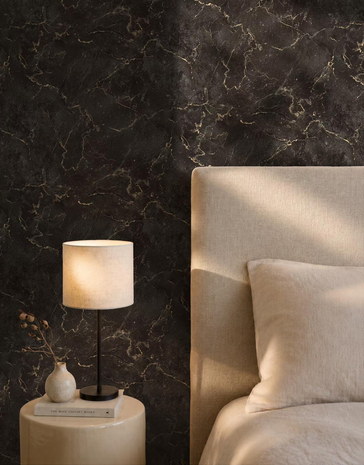 Black marble-effect wallpaper with gold veining behind a linen headboard and a cream bedside lamp