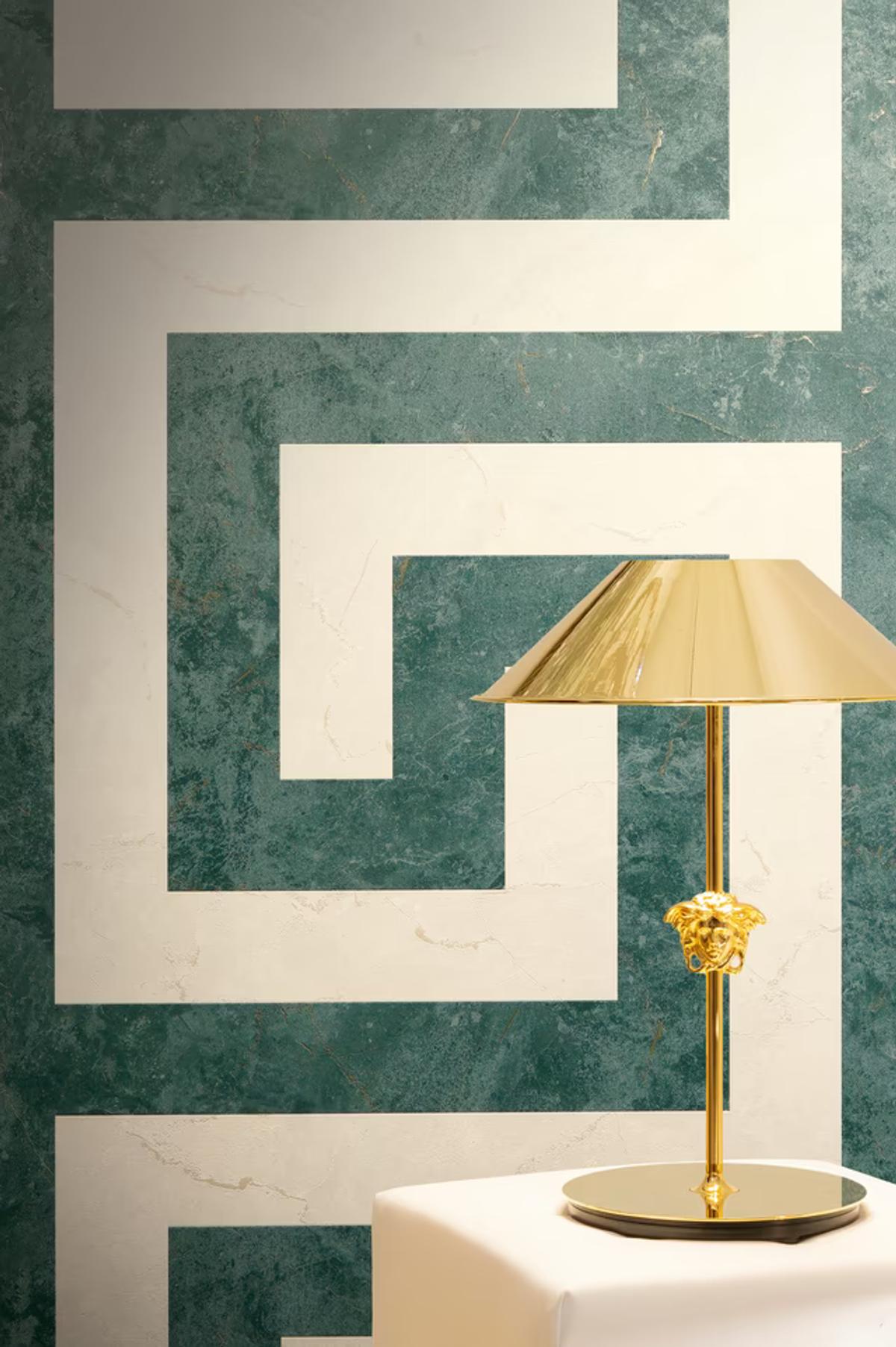 A Versace Greca key pattern in green marble and cream, with a gold Medusa table lamp in front