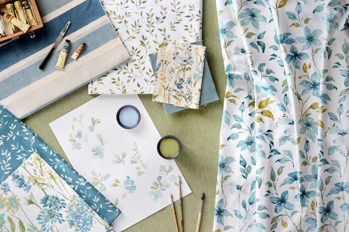 Fabric swatches, watercolour floral prints, paint pots and brushes laid out on sage linen