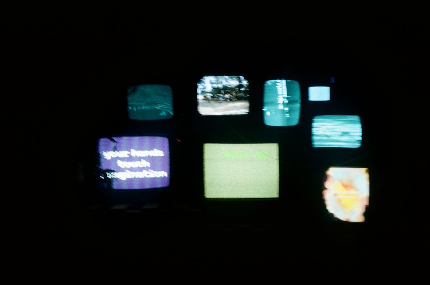 Blurry picture of multiple CRT televisions displaying generative visuals and text