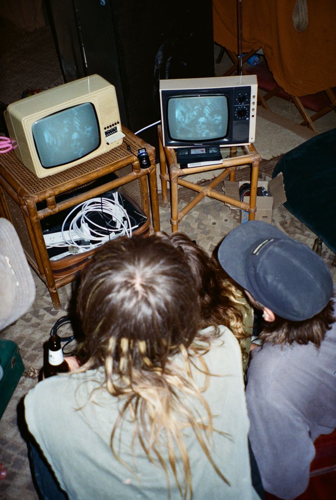 Two visitors seated on the floor watching themselves on vintage CRT televisions