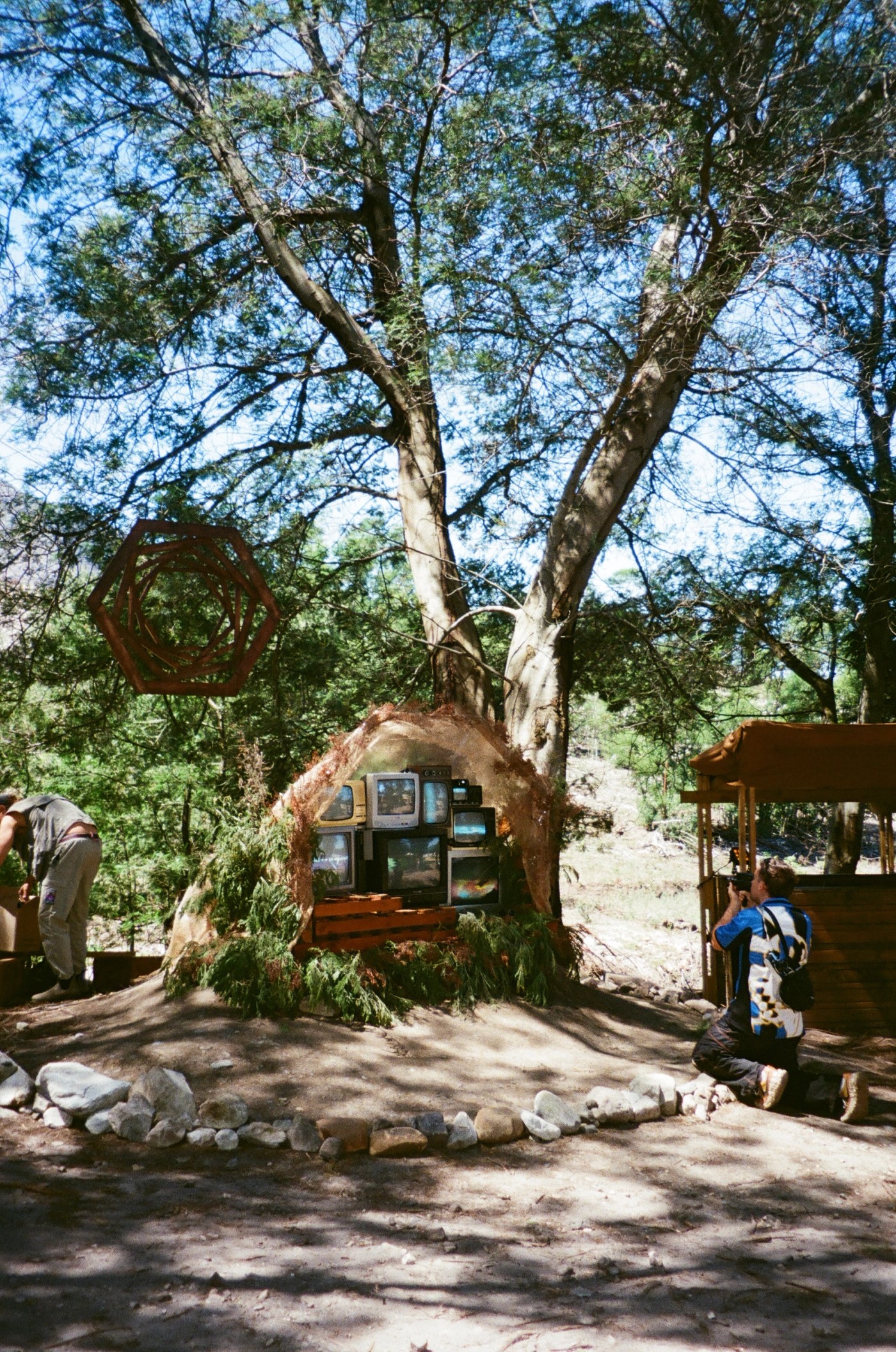 Person taking photograph of CRT television stack installed in an earthen dome at an outdoor festival