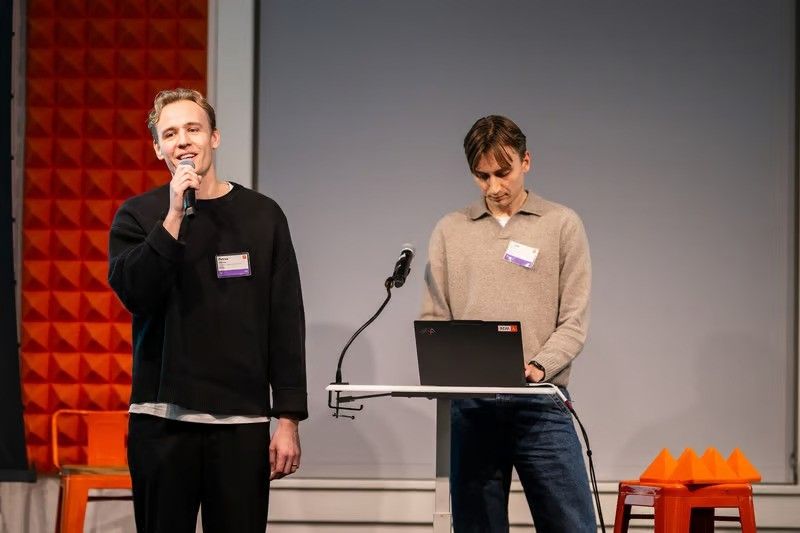 Two people presenting on stage, one speaking into a microphone