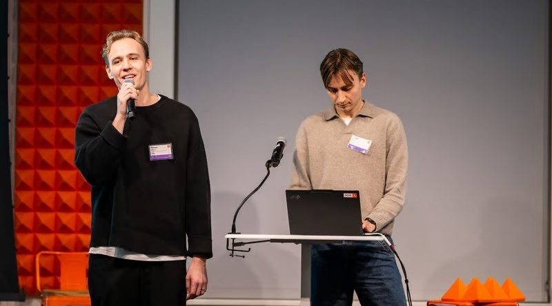Two people presenting on stage, one speaking into a microphone