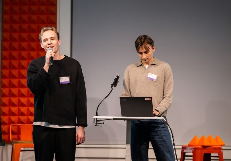 Two people presenting on stage, one speaking into a microphone