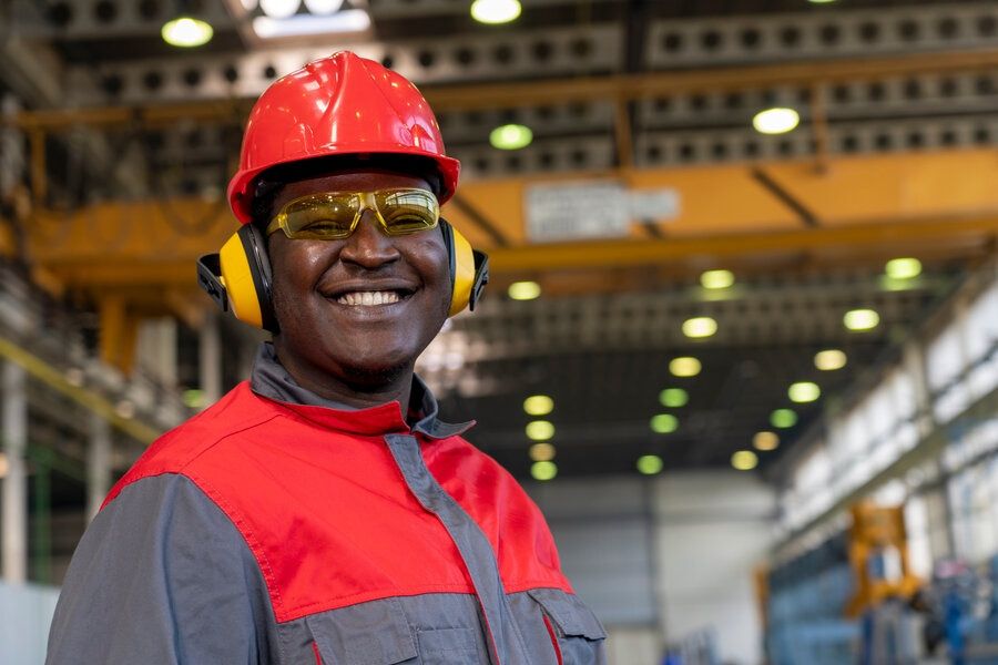 Smiling young African American worker in industrial setting wearing hearing protection