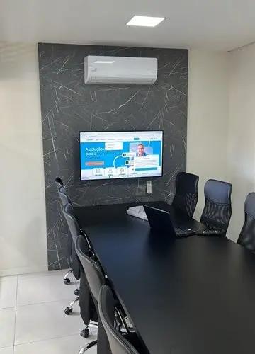 Sala de reunião corporativa com mesa longa, cadeiras ergonômicas, notebook e tela de apresentação na parede