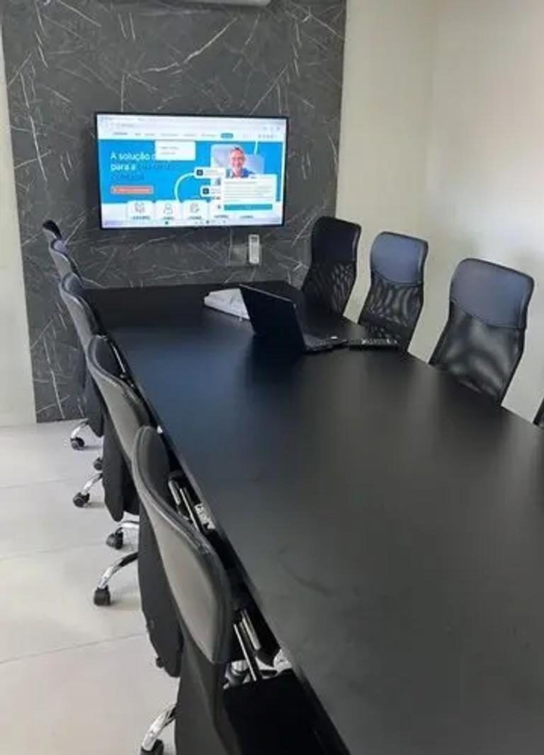 Sala de reunião moderna com mesa ampla, cadeiras ergonômicas e tela para apresentações