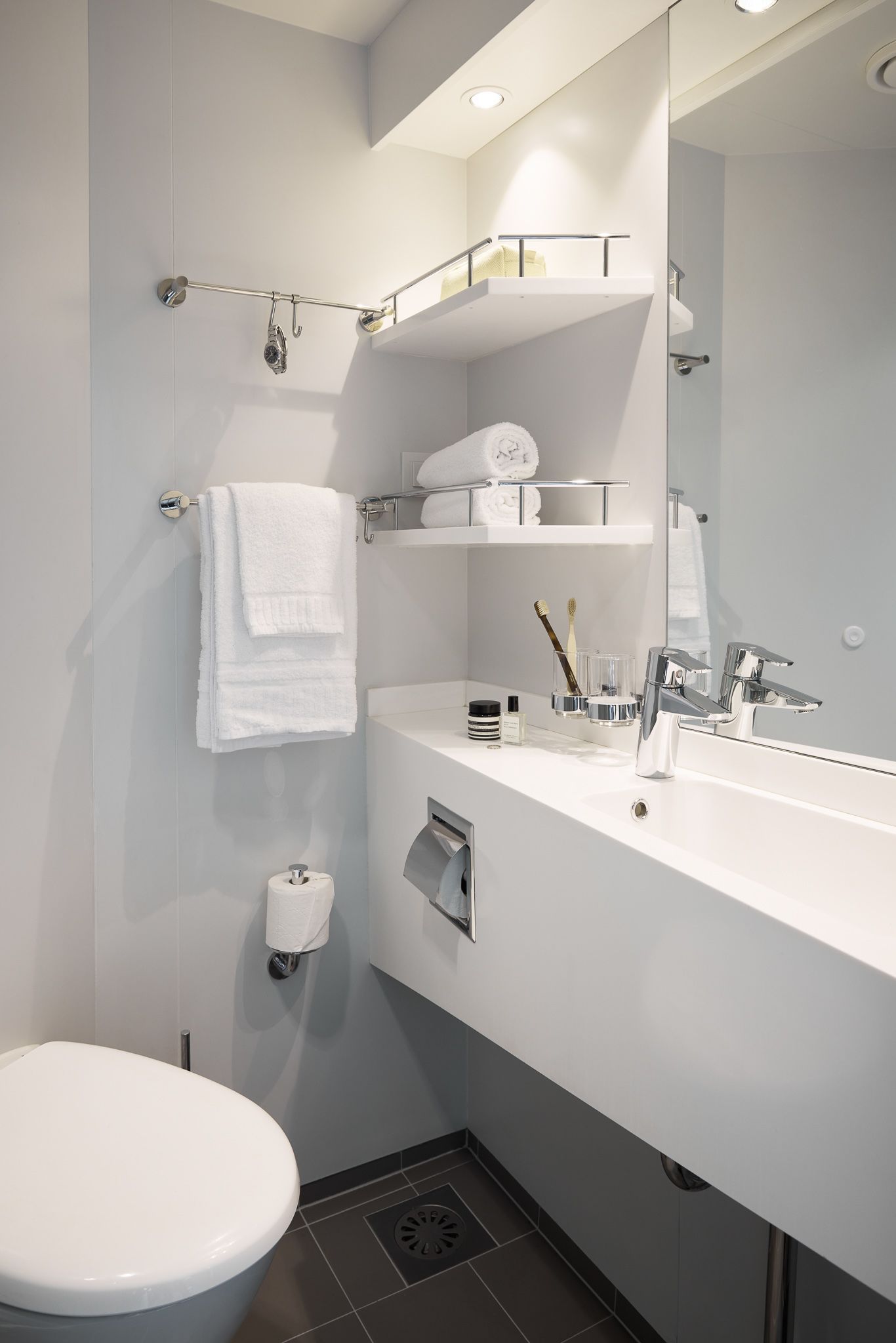 Modern bathroom with a large mirror, vanity sink, open shelving, fresh towels, and complimentary toiletries.