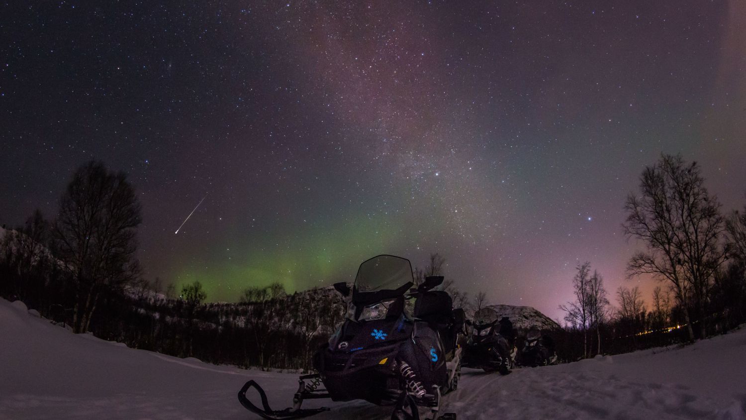 Snöskoter under en stjärnklar norrskenshimmel i Norge