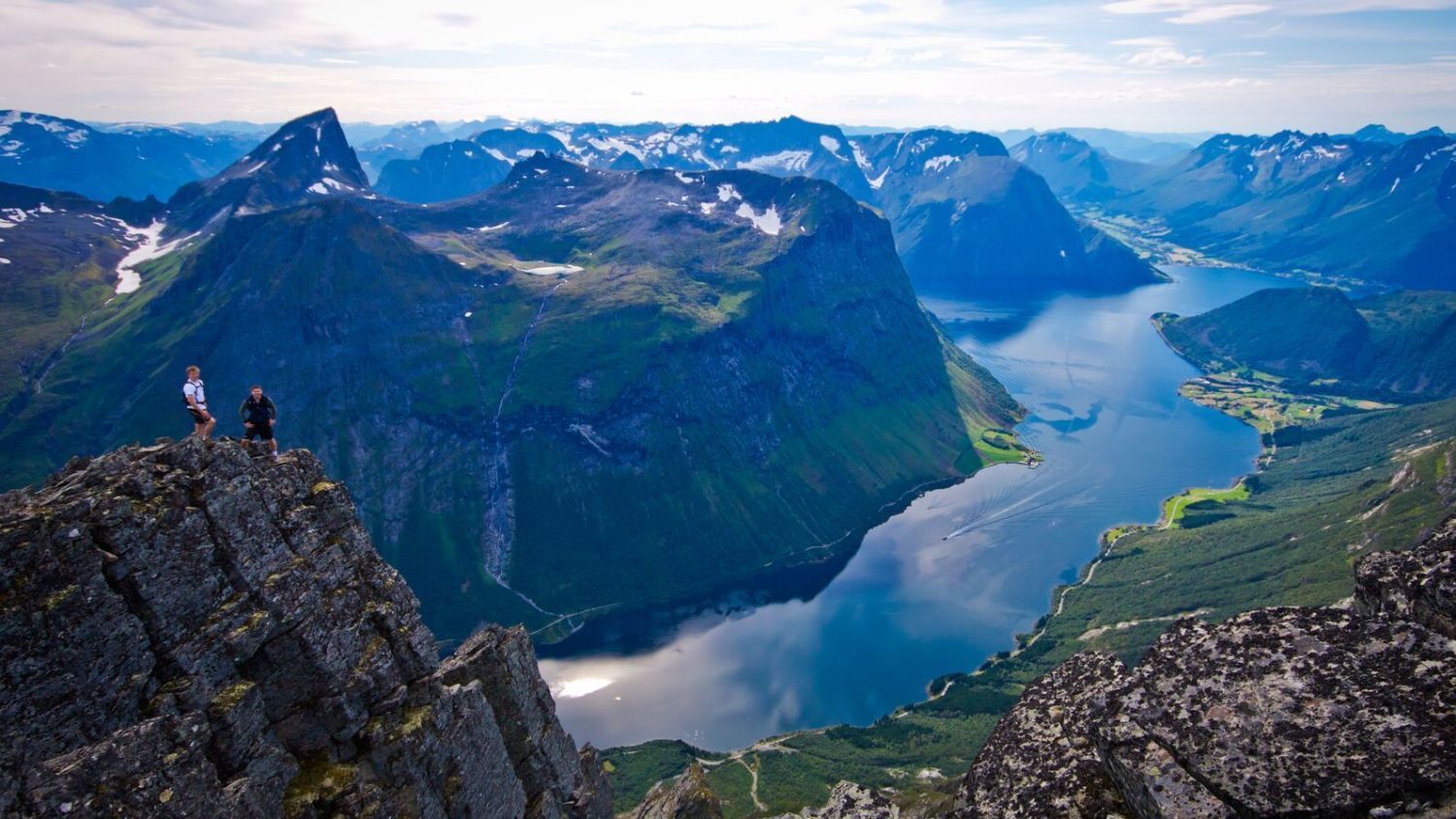 Wanderer genießen den atemberaubenden Ausblick vom Slogen über den Hjørundfjord, umgeben von den majestätischen Sunnmøre-Alpen und den unberührten norwegischen Fjorden.