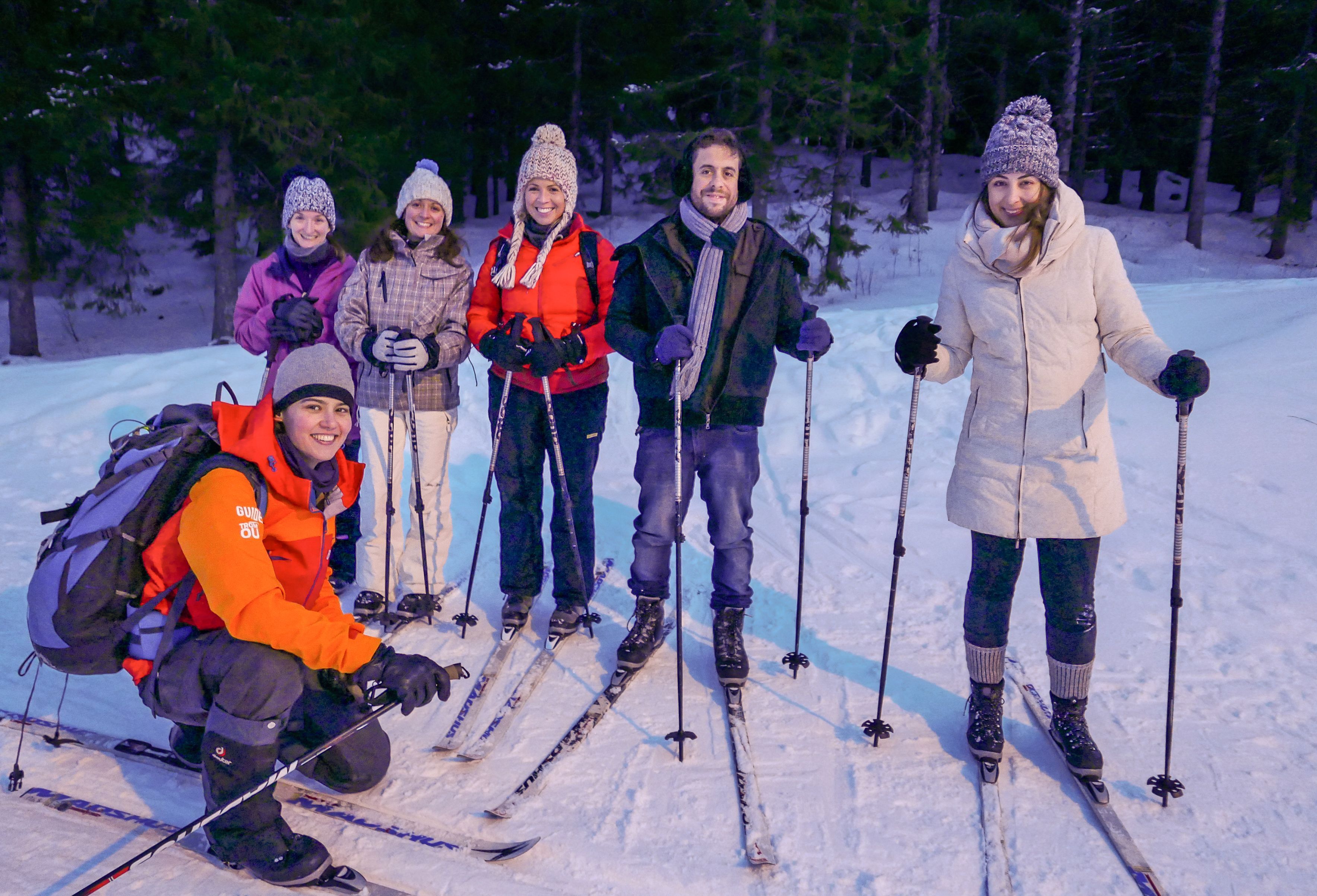 Gjester og deres guide poserer sammen på langrennsski i en snødekt skog nær Tromsø etter en nybegynneropplevelse på ski, kledd i varme vinterklær og smilende i det arktiske skumringslyset.