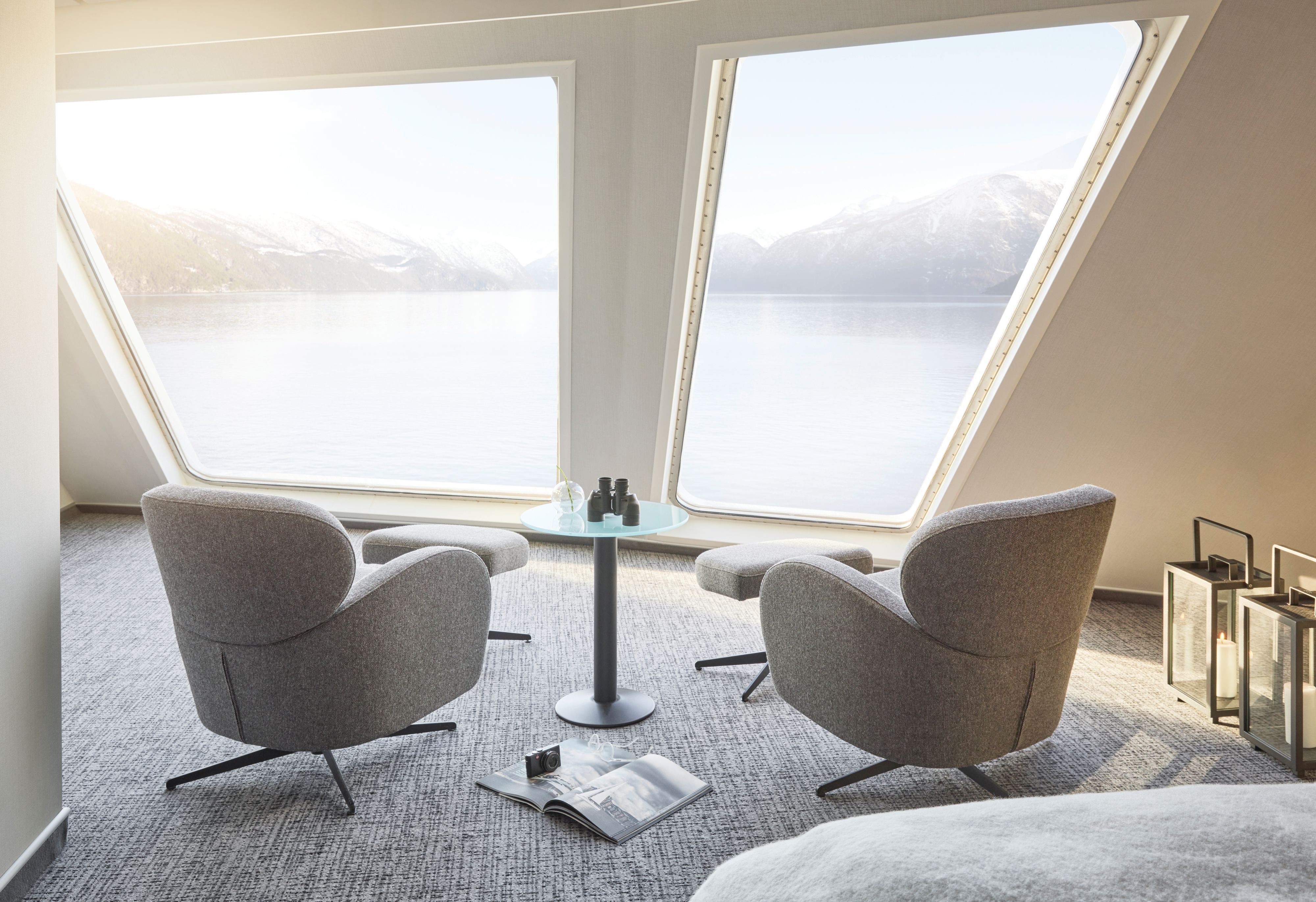 Loungeområde i Panoramic Corner Mini Suite med to lenestoler, et lite bord, panoramavinduer fra gulv til tak og storslått utsikt over den norske kystlinjen.