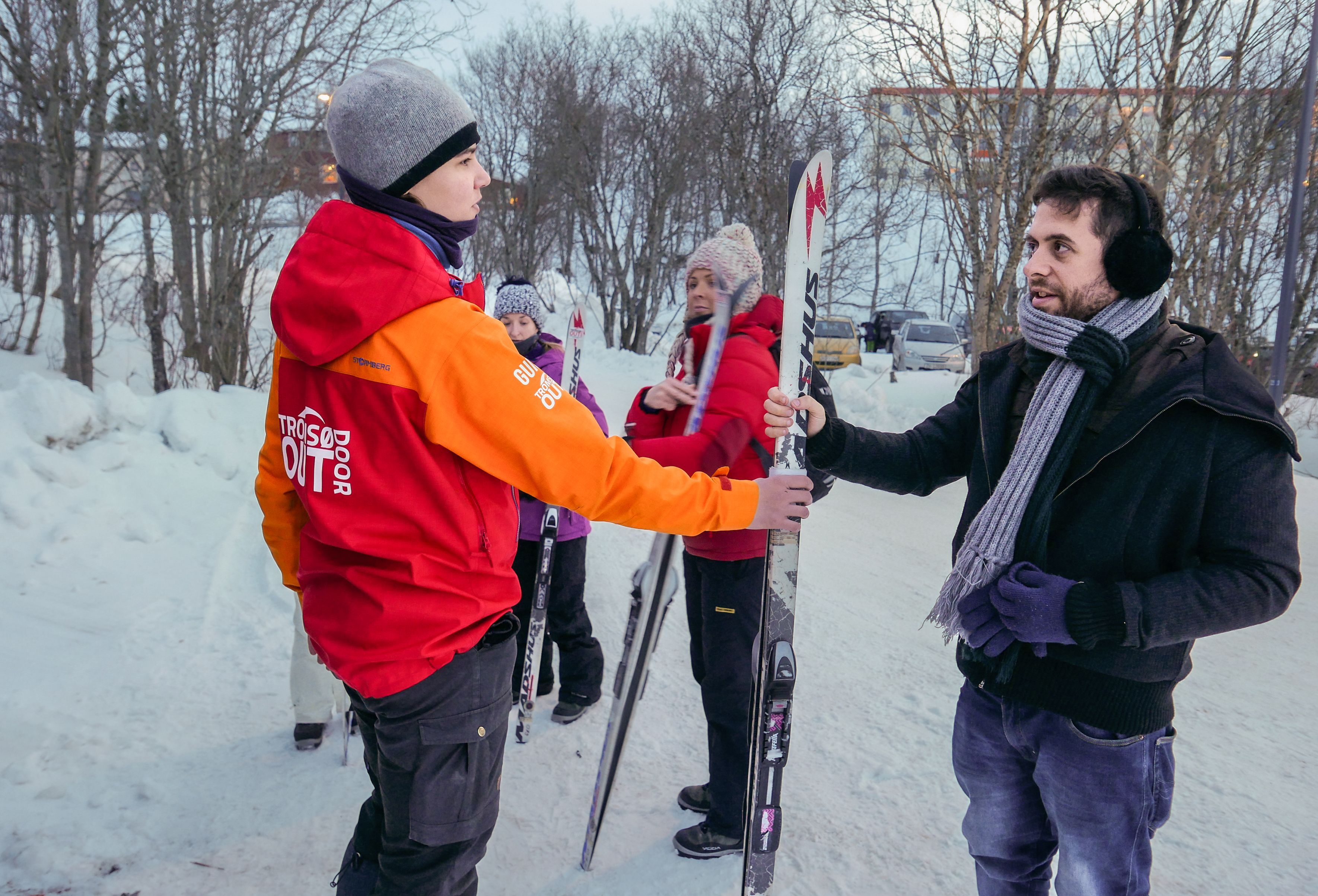 Guide som hjelper en gjest med langrennsutstyr før en nybegynnertime i ski i Tromsø, mens andre deltakere gjør seg klare i bakgrunnen.