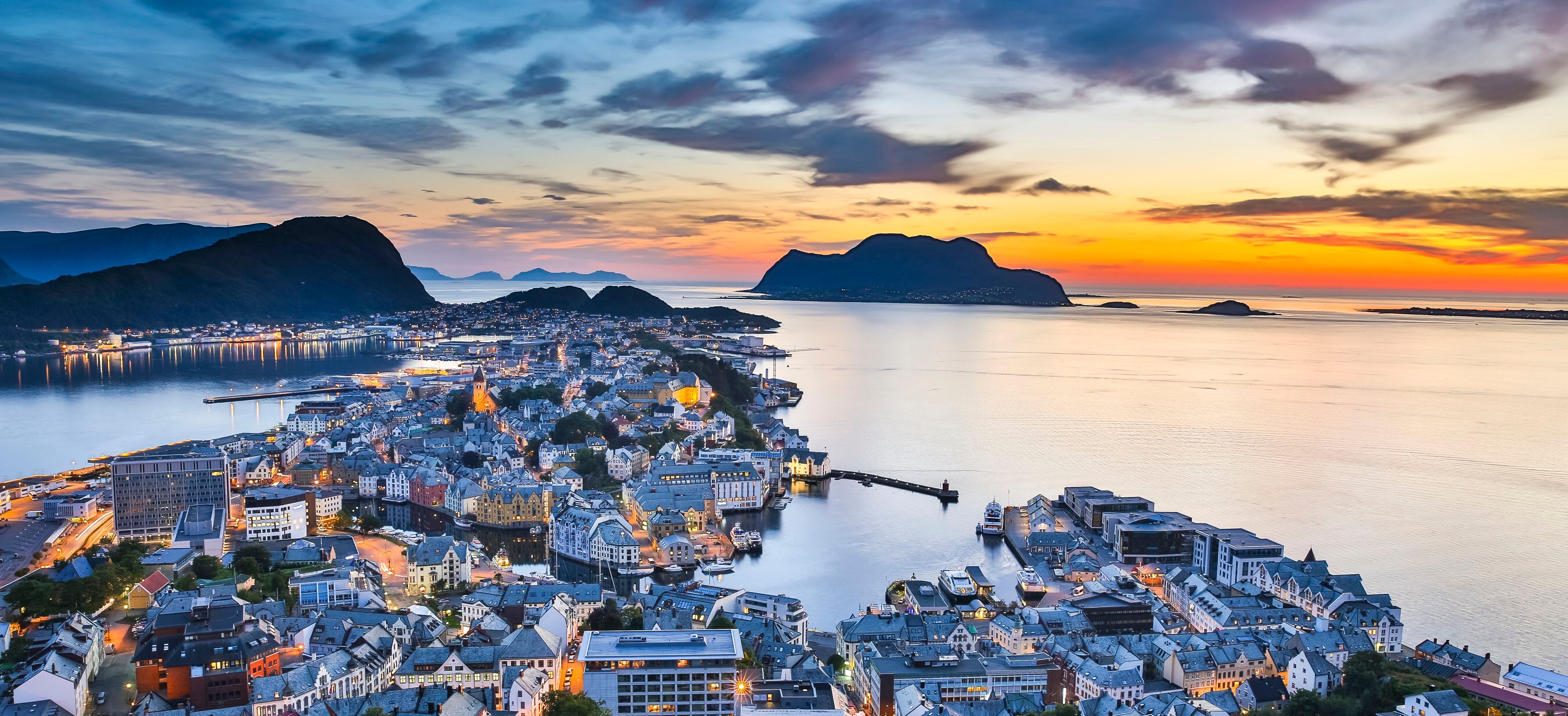 Panoramablick auf Ålesund vom Berg Aksla bei Sonnenuntergang, mit Blick auf die Jugendstilstadt, die umliegenden Inseln, das ruhige Fjordwasser und einen farbenfrohen Abendhimmel.