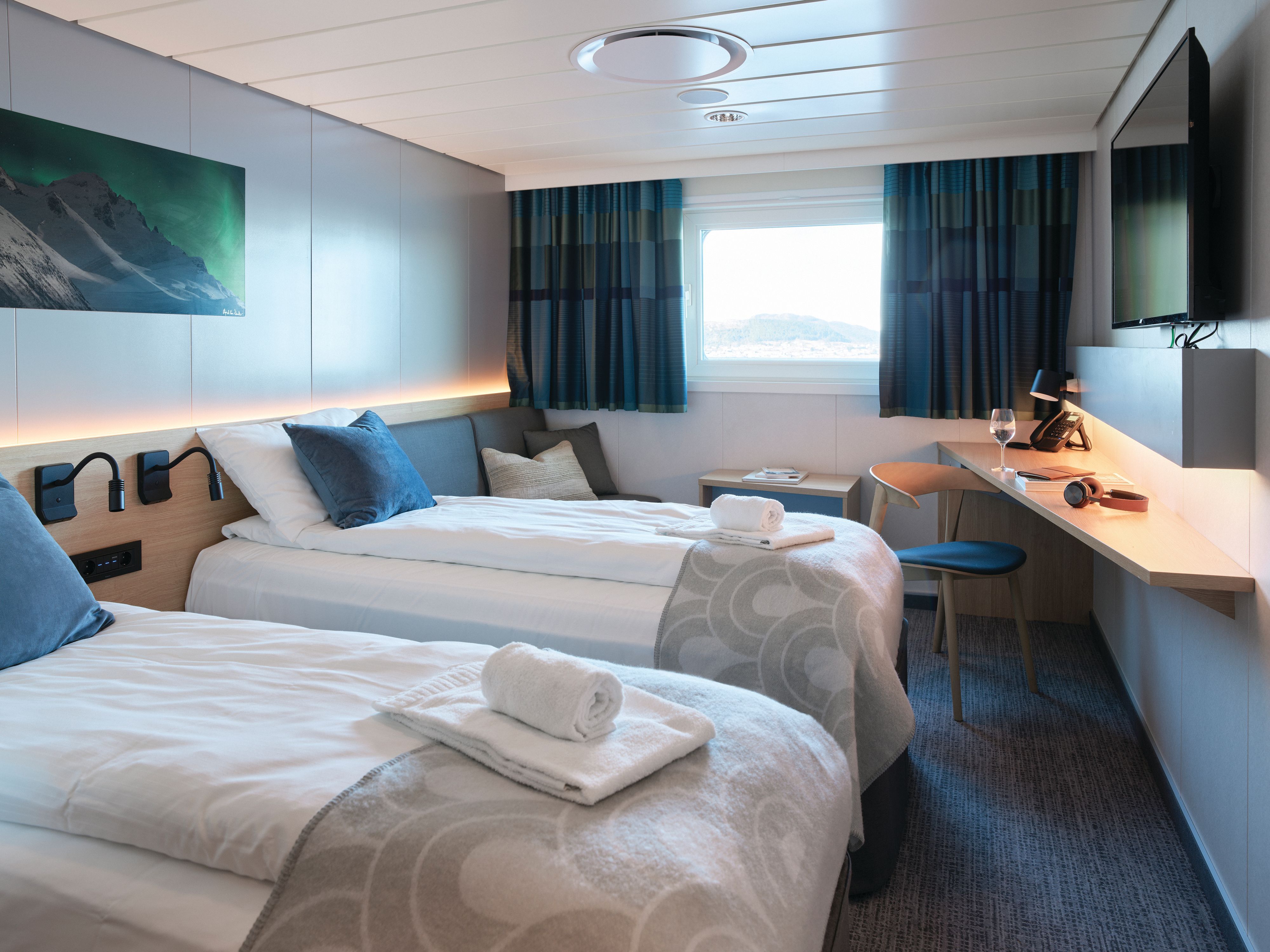 Superior-Kreuzfahrtkabine Seaview Twin mit zwei Einzelbetten, großem Fenster, Schreibtisch, Kleiderschrank, TV und gemütlicher Sitzecke.