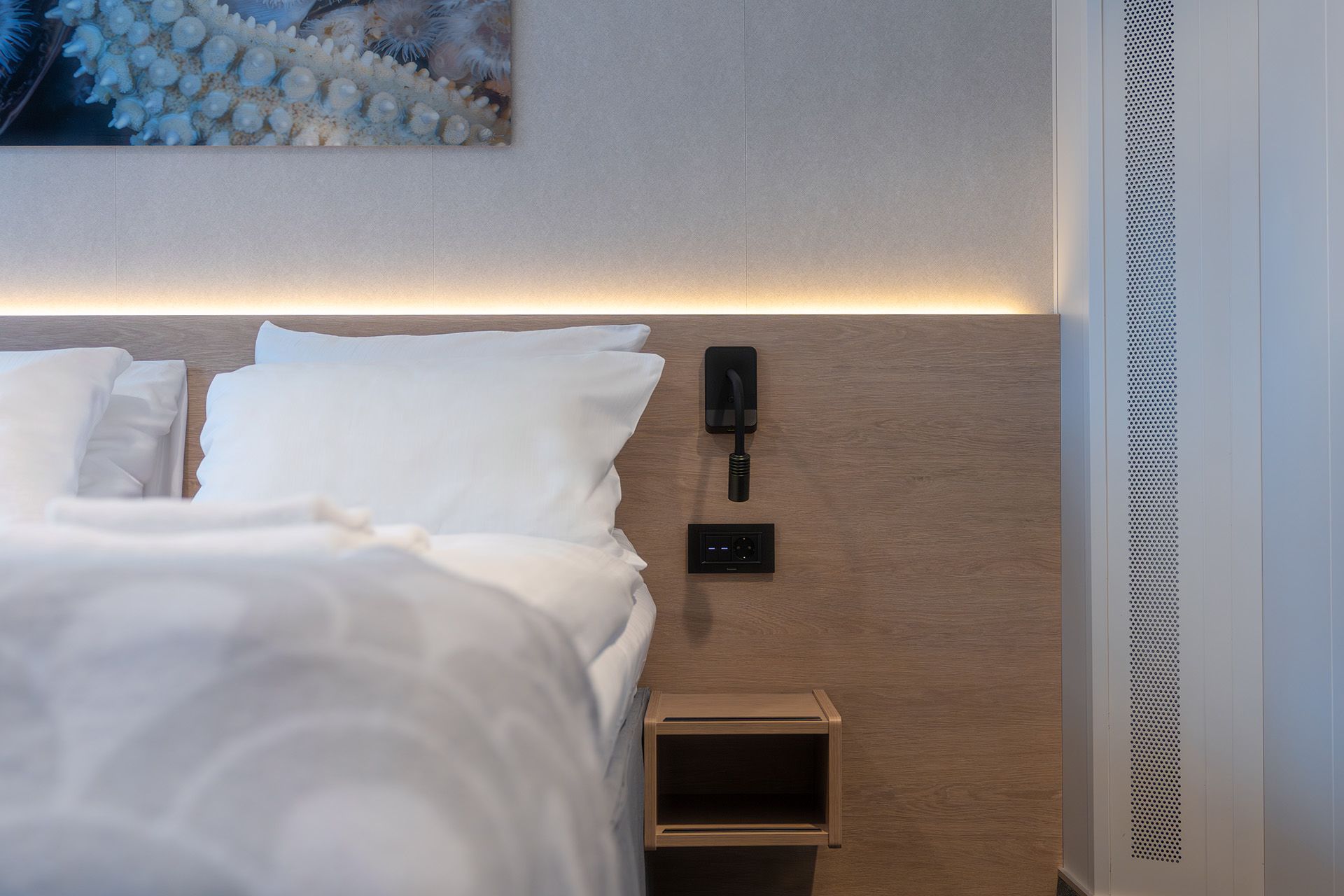 Aft View Superior Double cruise cabin bedside with reading light, power outlet, bedside shelf, and modern Scandinavian design.