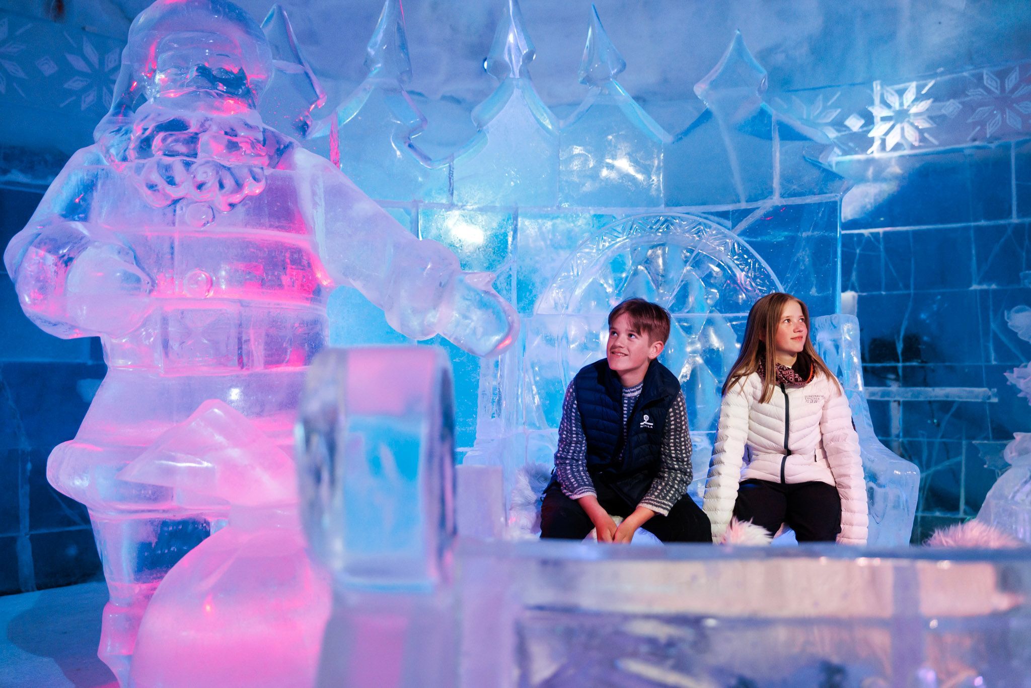 To barn som beundrer fargerike isskulpturer inne på Snowhotel Kirkenes.