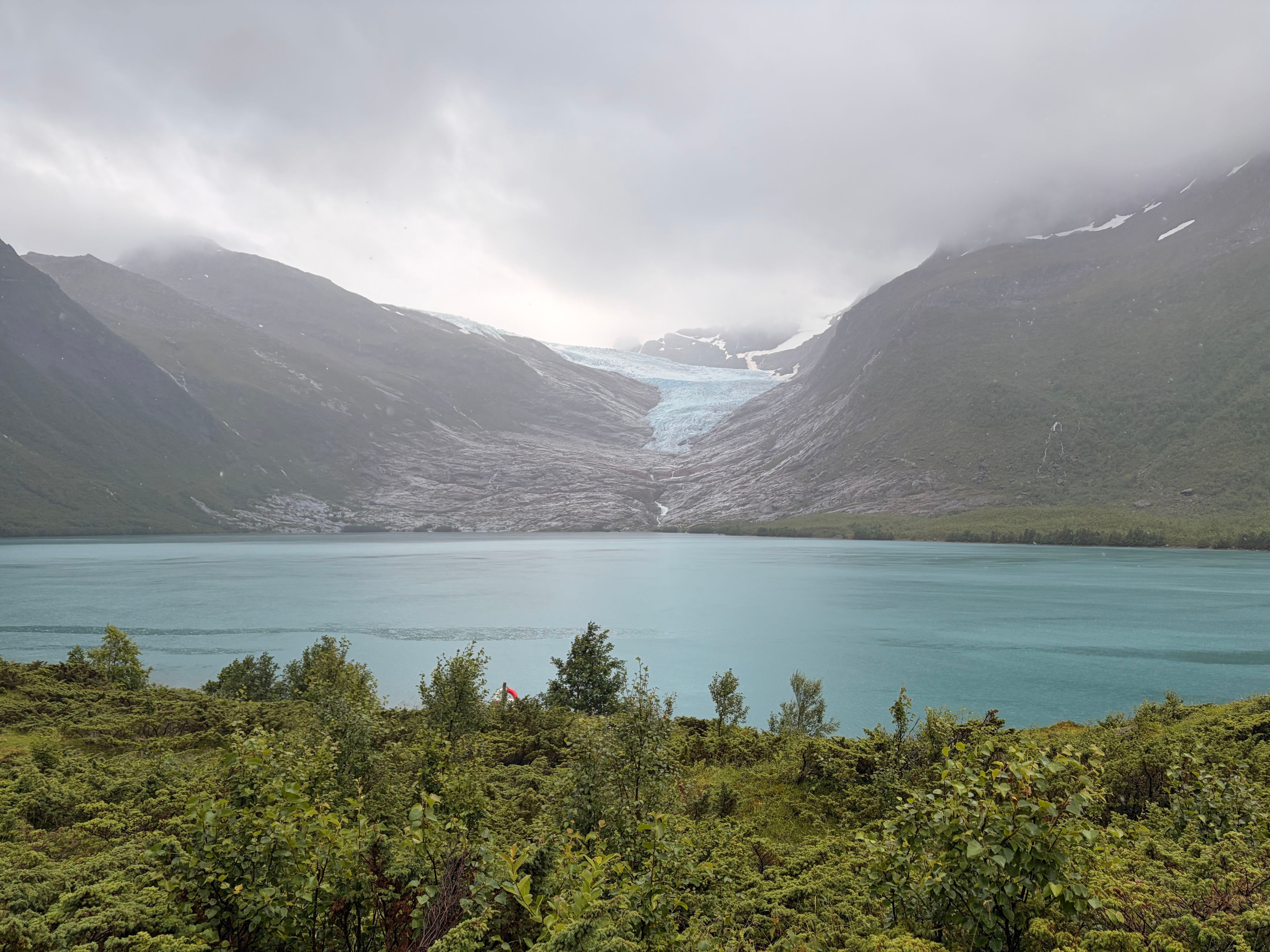 Der Gletscherarm Engabreen des Svartisen, der sich unter tief hängenden Wolken zum türkisfarbenen Gletschersee Engabrevatnet hinabzieht, Nordland, Norwegen