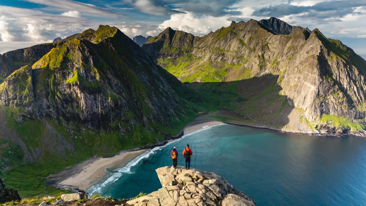 Två vandrare står på en klippavsats och blickar ut över den fantastiska utsikten mot Ryten Kvalvika Beach.