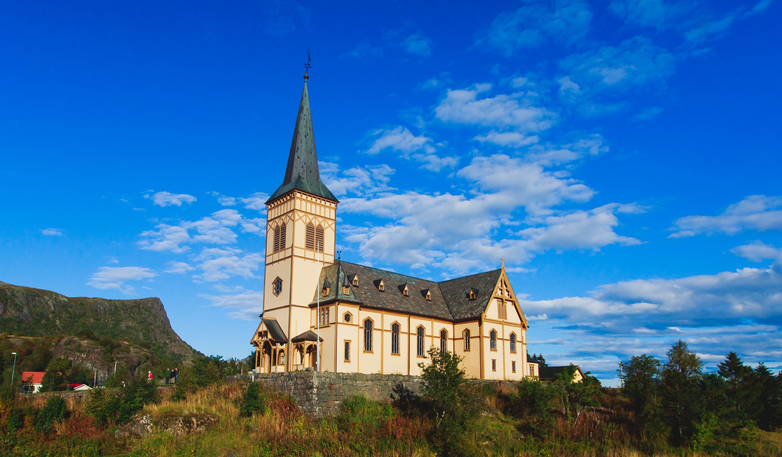 Lofotenkatedralen, en stor gul träkyrka med ett högt torn, på en kulle under en klarblå himmel i Kabelvåg, Norge