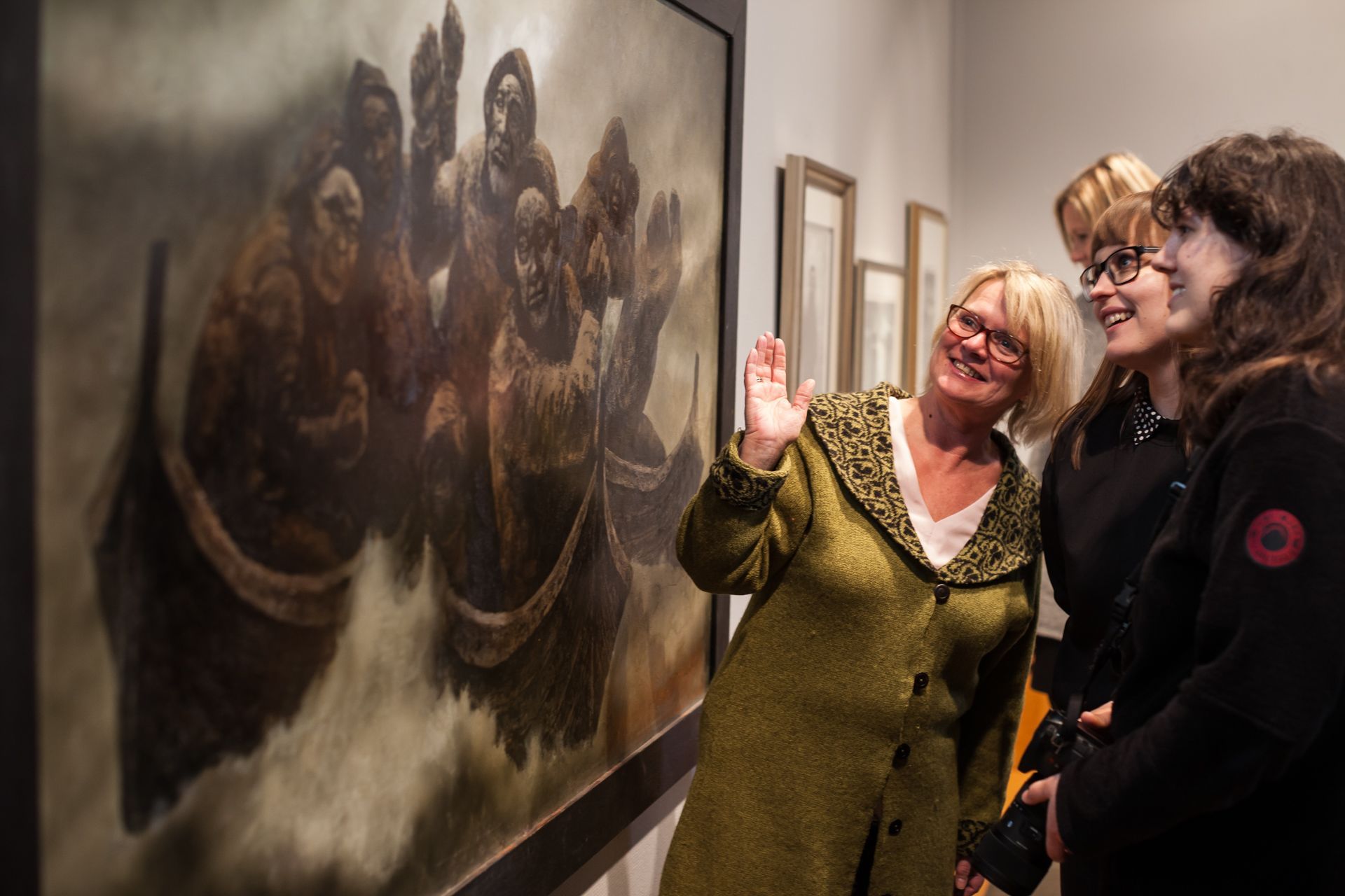 Guide gesturing toward a large painting of fishermen while visitors listen during an art gallery tour in Lofoten, Norway