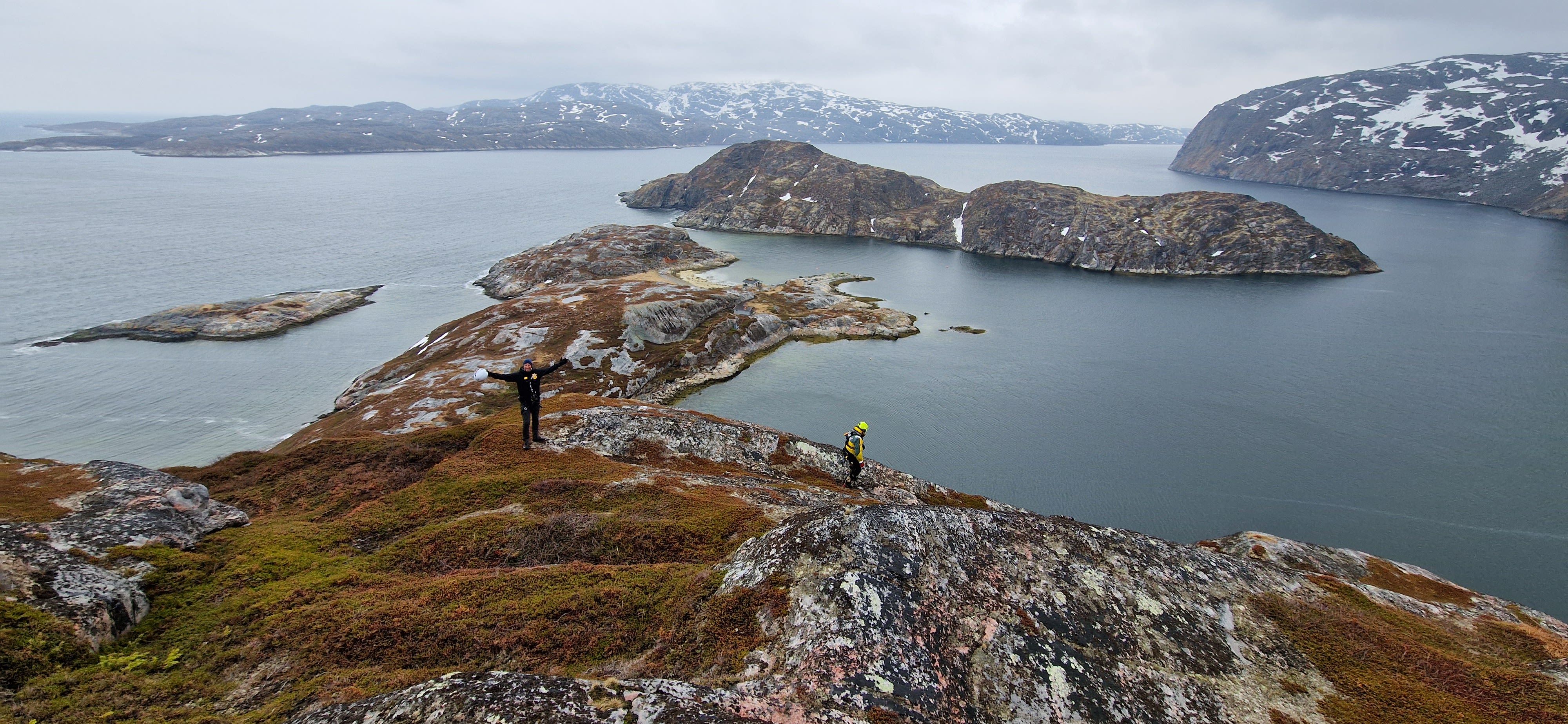 Panoramic view of participants hiking to the Arctic Rappelling Route above a dramatic fjord and rocky islands in Northern Norway.
