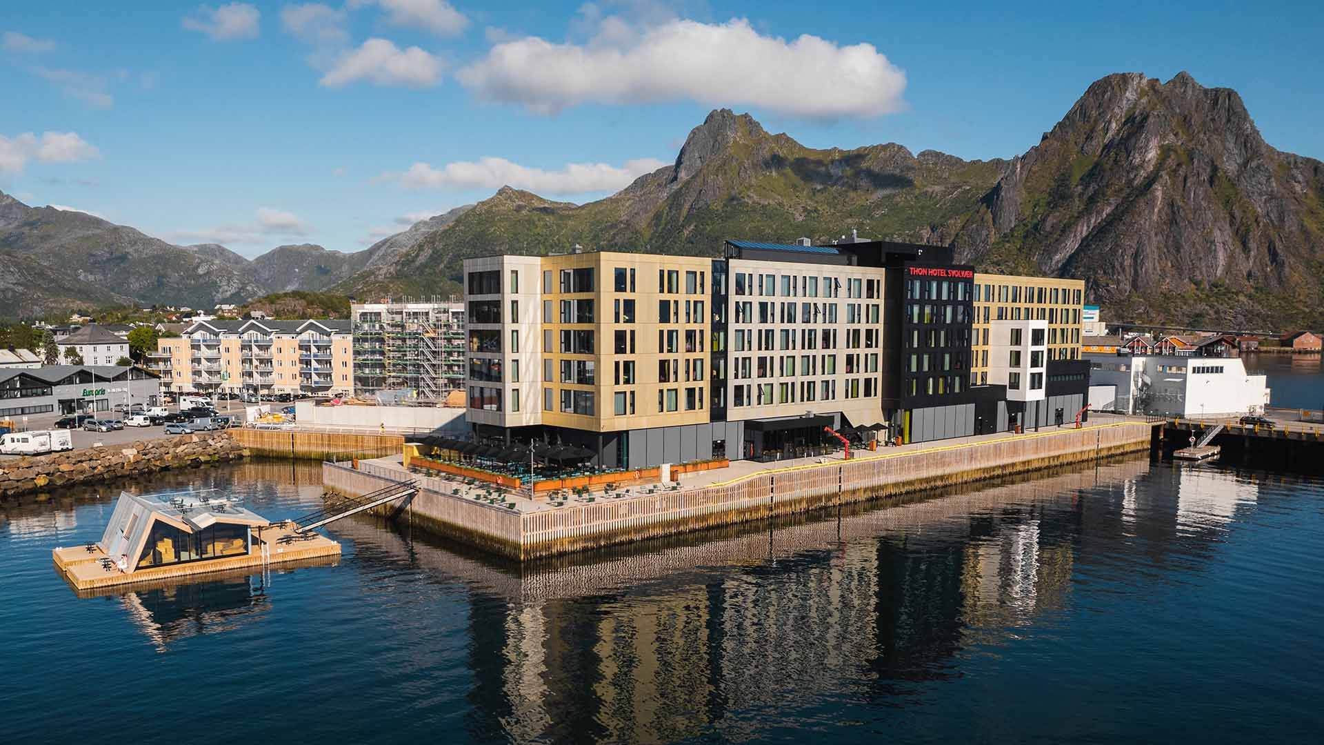 Sonnendurchflutete Berggipfel und tiefe Fjorde auf den Lofoten, die die spektakuläre Landschaft zeigen, die man während eines Küstenaufenthalts mit Havila Voyages erlebt.