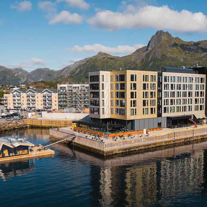 Sonnendurchflutete Berggipfel und tiefe Fjorde auf den Lofoten, die die spektakuläre Landschaft zeigen, die man während eines Küstenaufenthalts mit Havila Voyages erlebt.