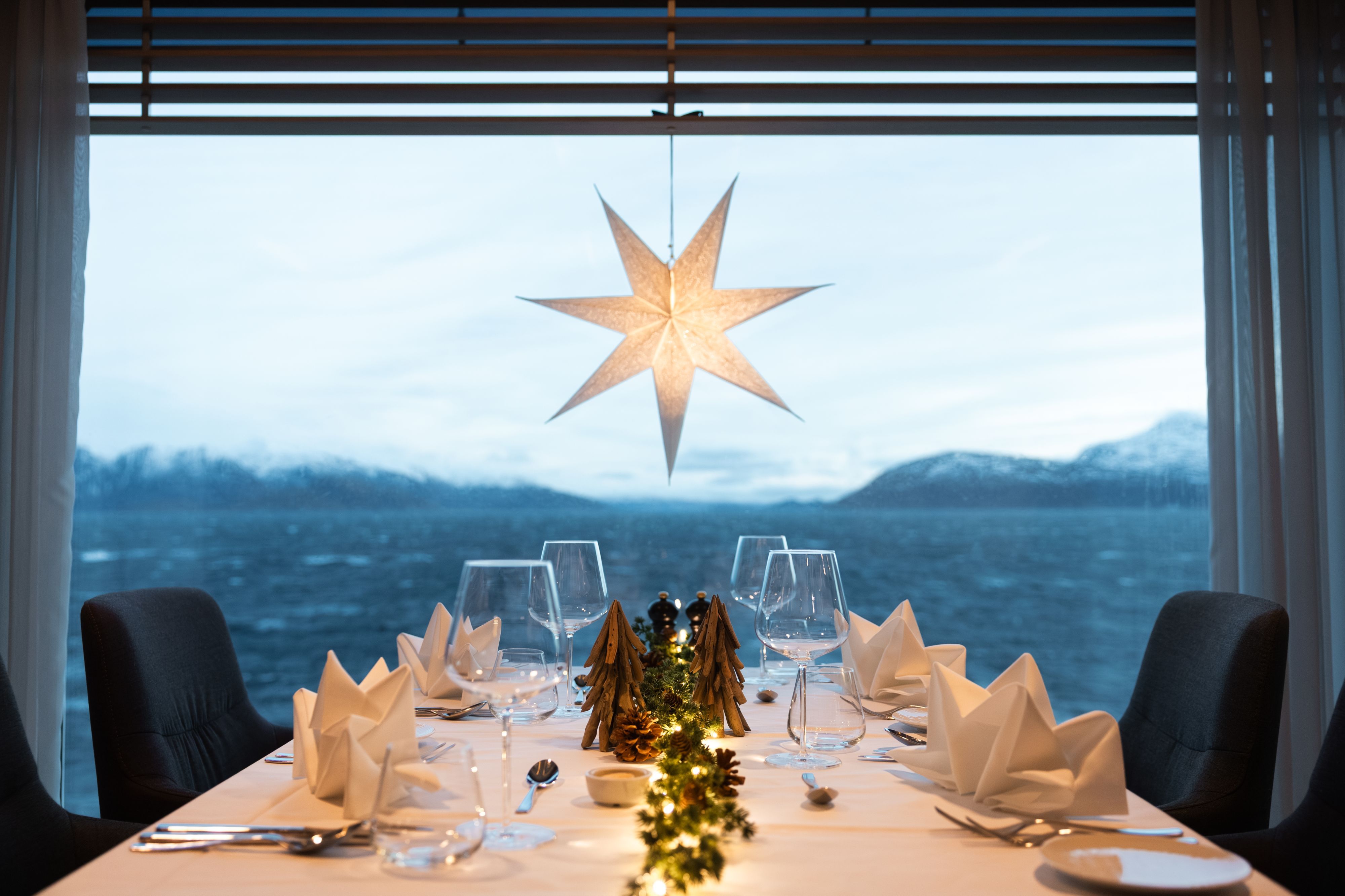 Festlig pyntet spisebord med panoramautsikt over fjorden om bord på Havila Kystruten, som viser ekte norske juletradisjoner til sjøs.