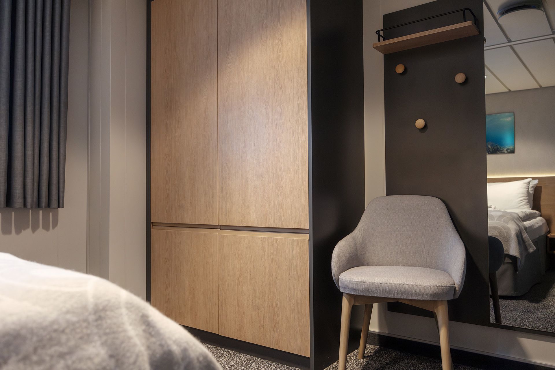 Garderobe- und Eingangsbereich der Aft View Mini Suite mit geräumigem Kleiderschrank, Ganzkörperspiegel, Garderobenhaken und einem bequemen Stuhl, während im Hintergrund das Schlafzimmer zu sehen ist.
