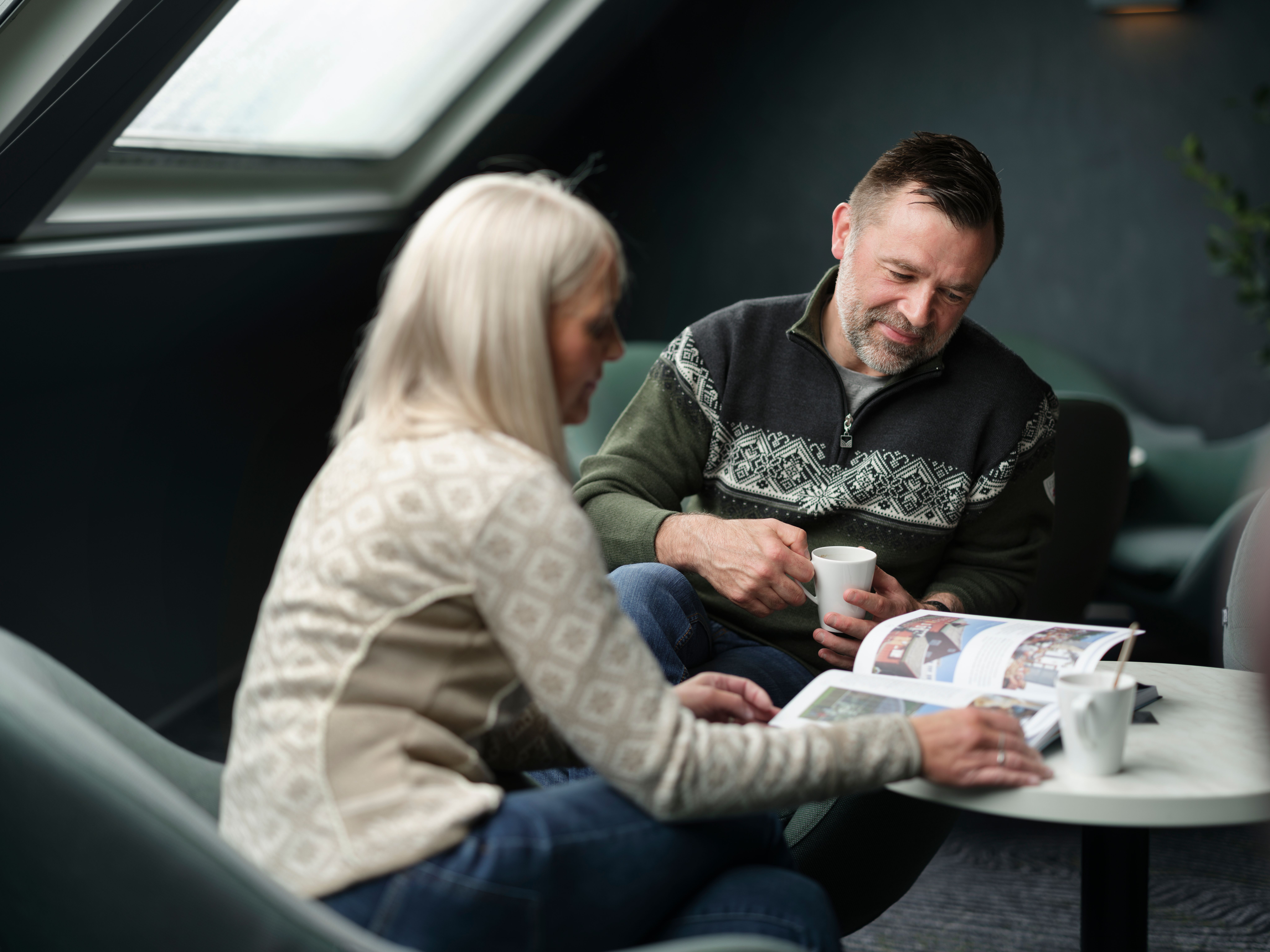 Par i stickade tröjor som bläddrar i en tidning över en kopp kaffe i fartygets lounge