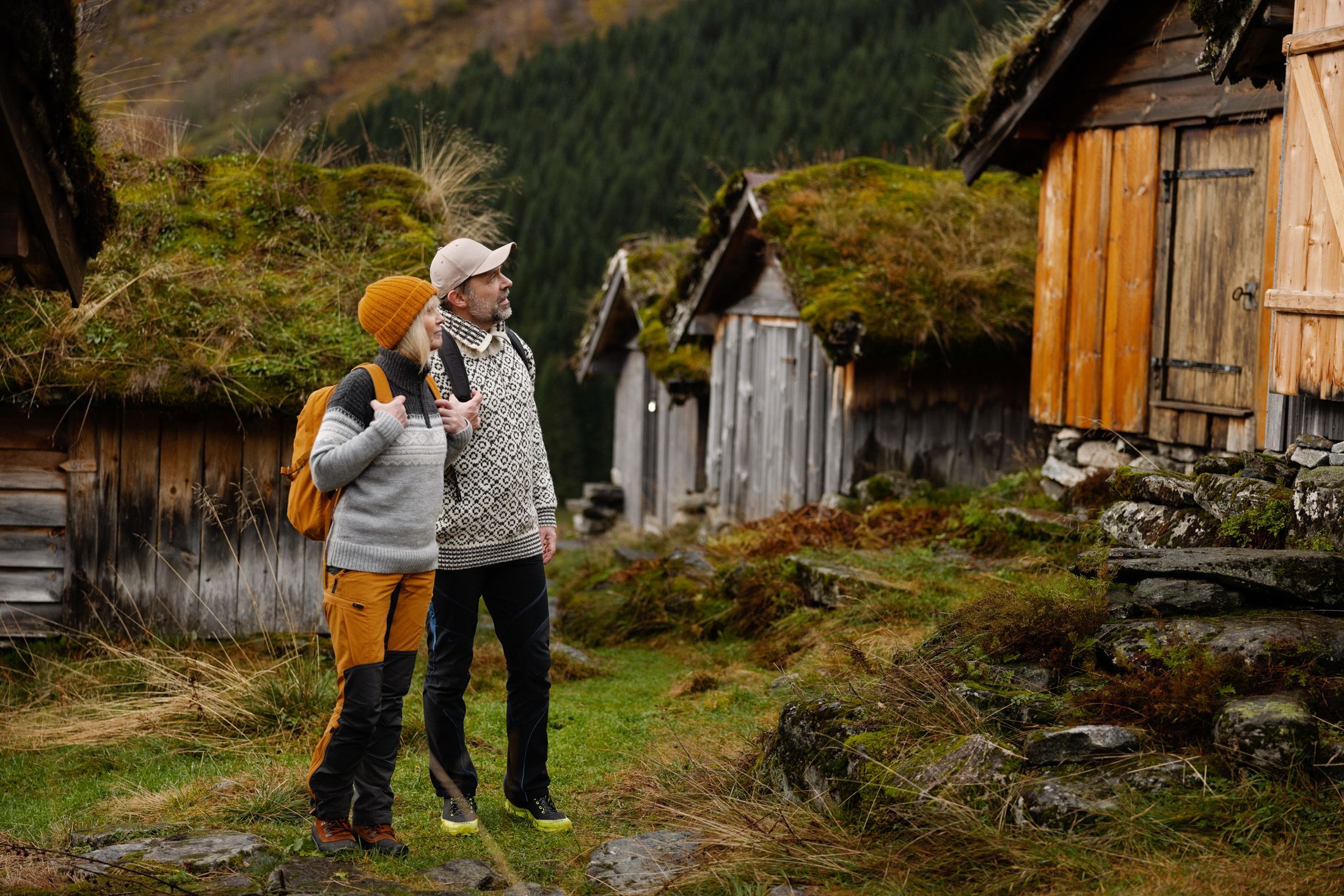 Besøkende som utforsker tradisjonelle fjellgårdsbygninger med torvtak i en naturskjønn norsk dal